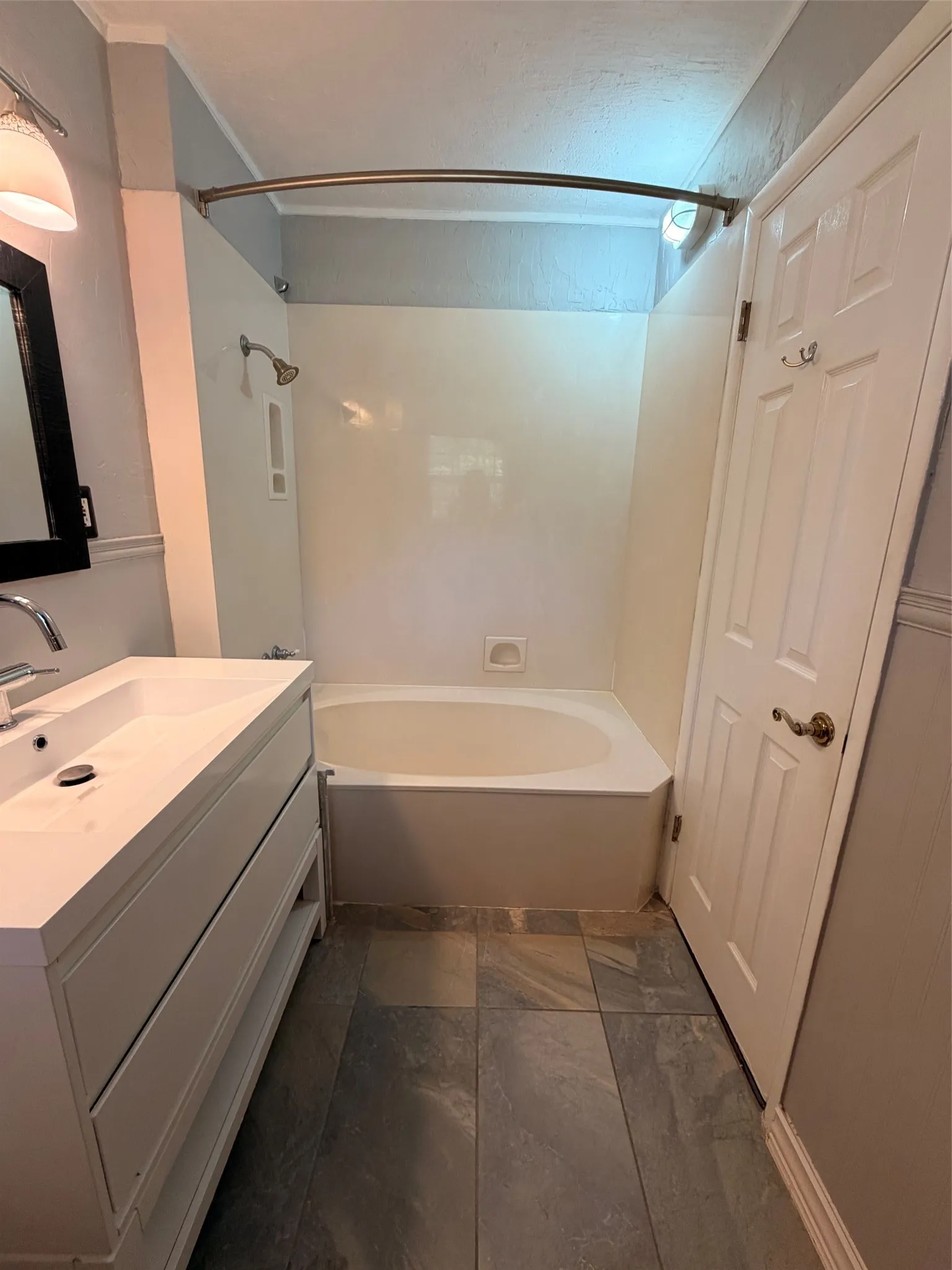White vanity with integrated sink, modern faucet, built-in bathtub, shower fixture, and gray tile flooring