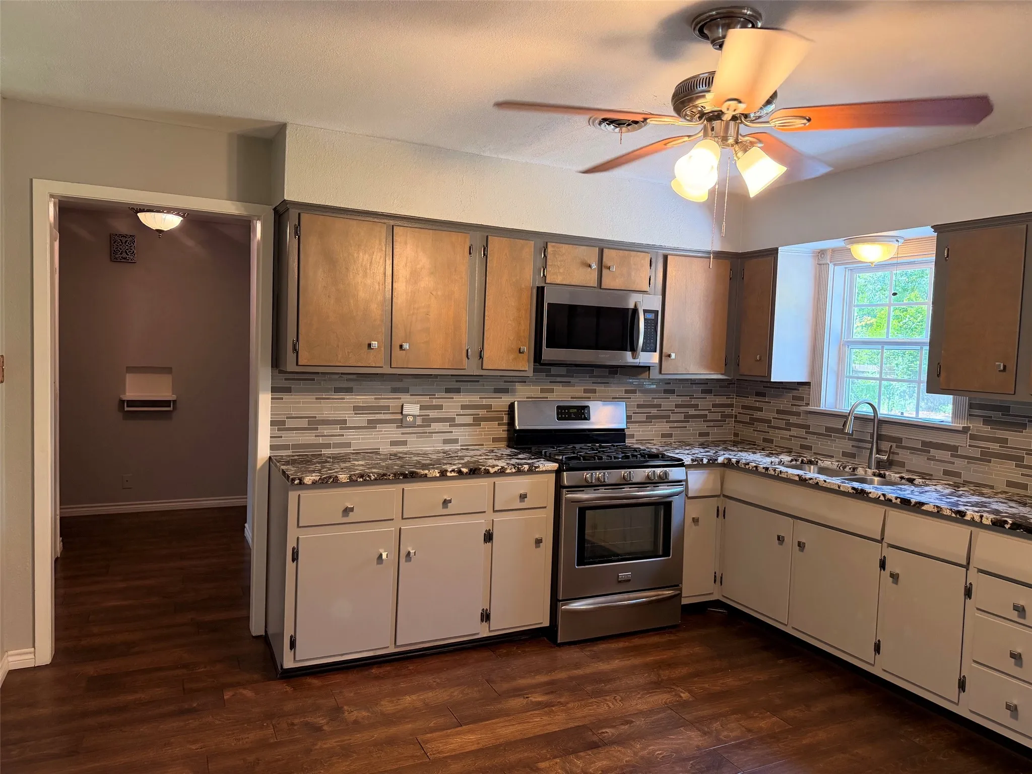 Kitchen featuring wood-finish flooring, a mosaic tile backsplash, stainless steel appliances, a ceiling fan with integrated lighting, and a window above the sink