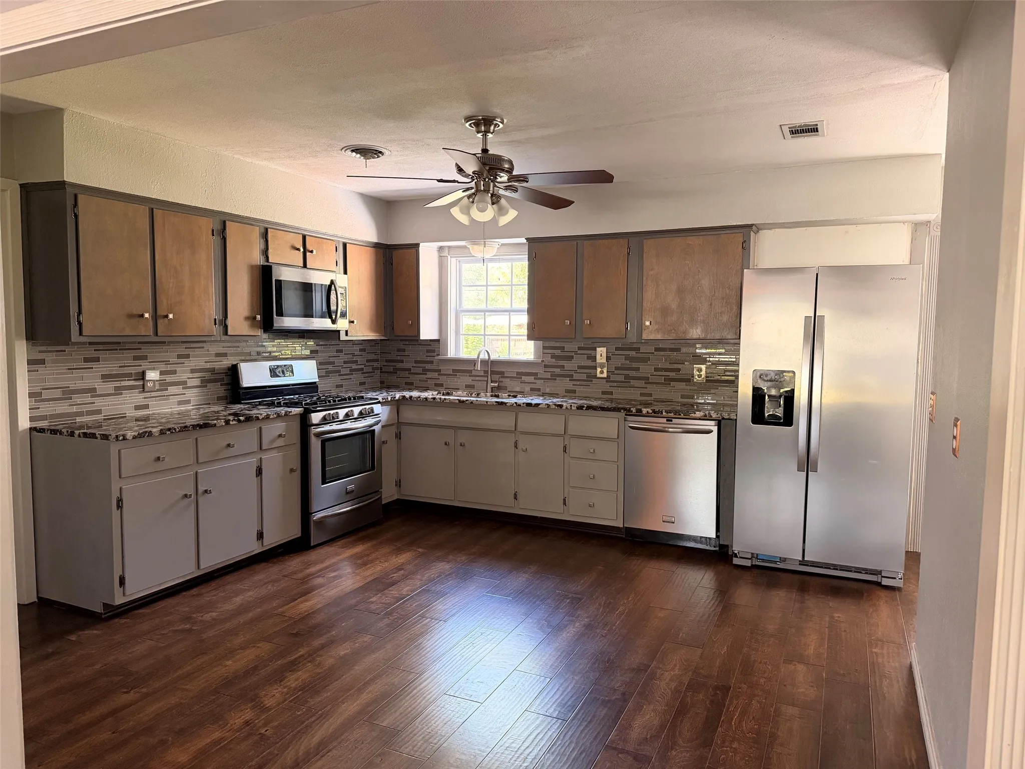 Kitchen featuring wood-finish flooring, granite countertops, stainless steel appliances, a tiled backsplash, and a ceiling fan