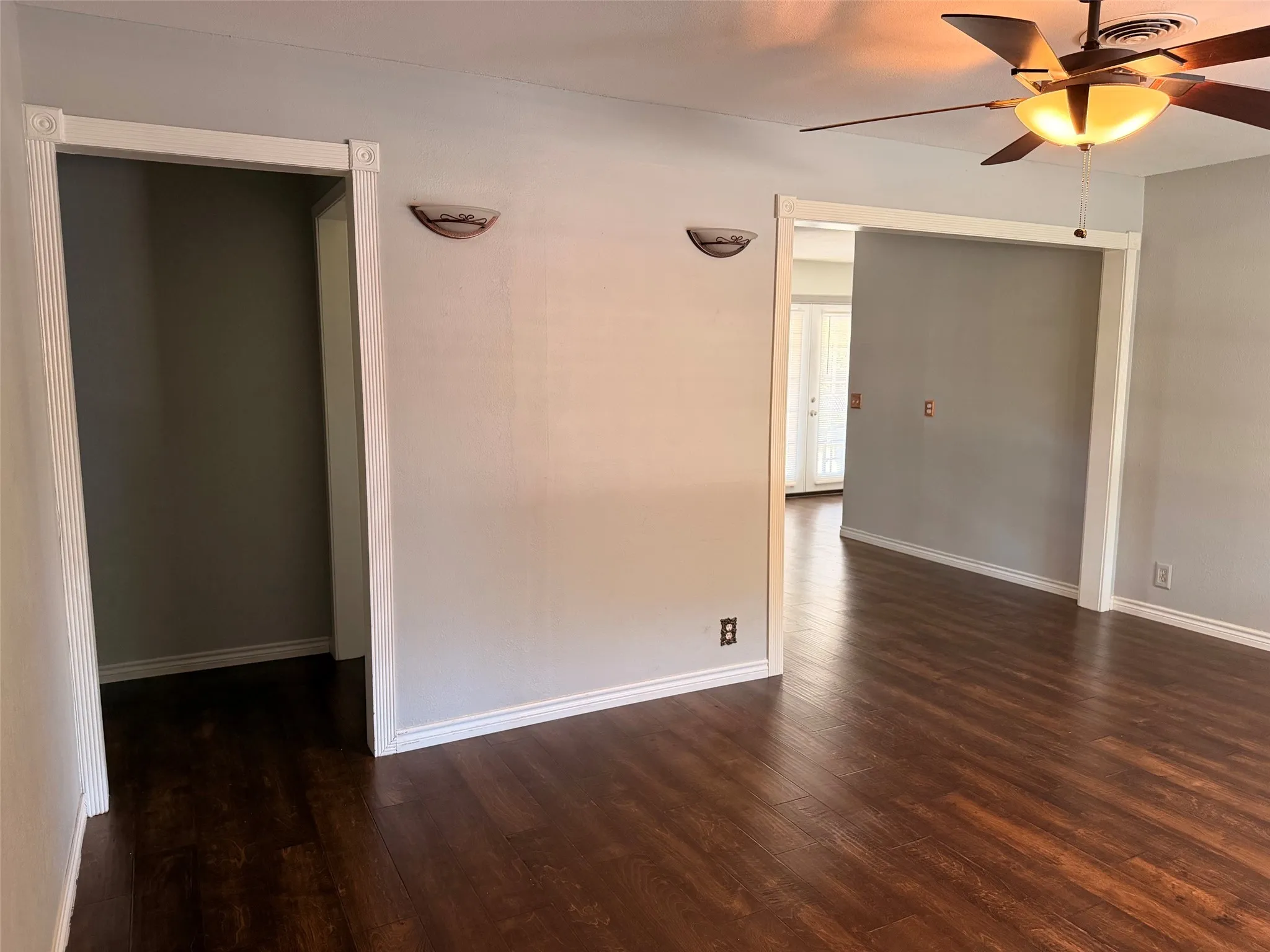 Dark wood-finish flooring, ceiling fan with integrated lighting, two wall sconces, and white trim work