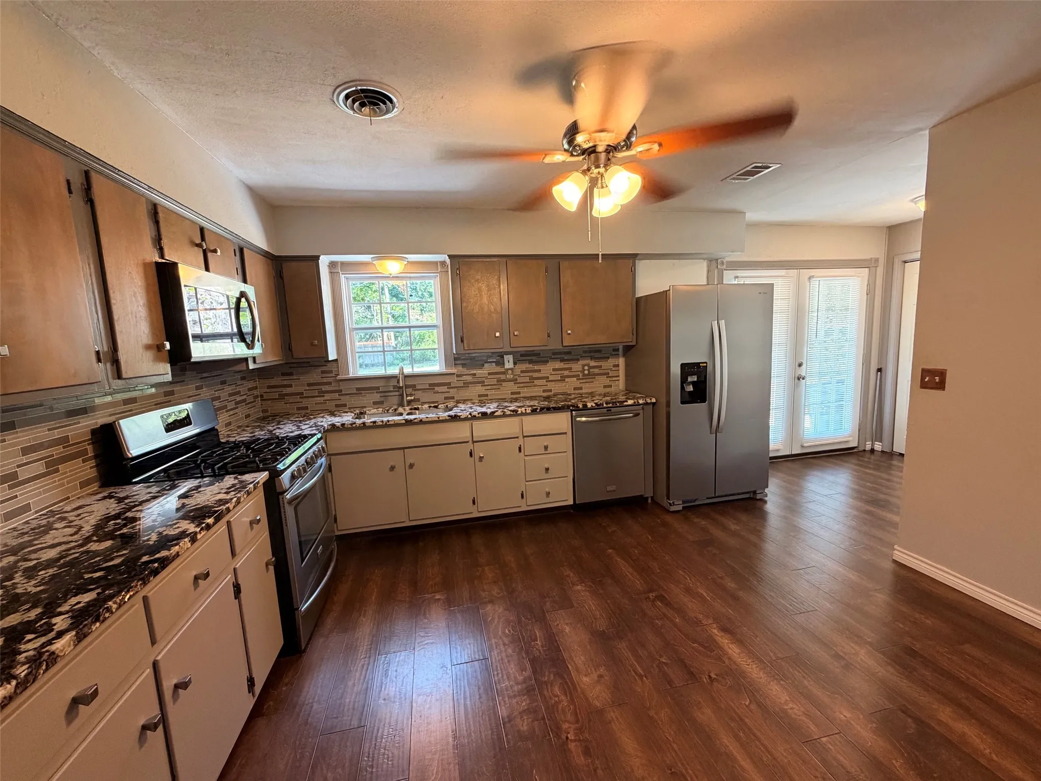 Kitchen featuring wood-finish flooring, dark wood-finish cabinetry, patterned backsplash, a stainless steel gas range, and French doors