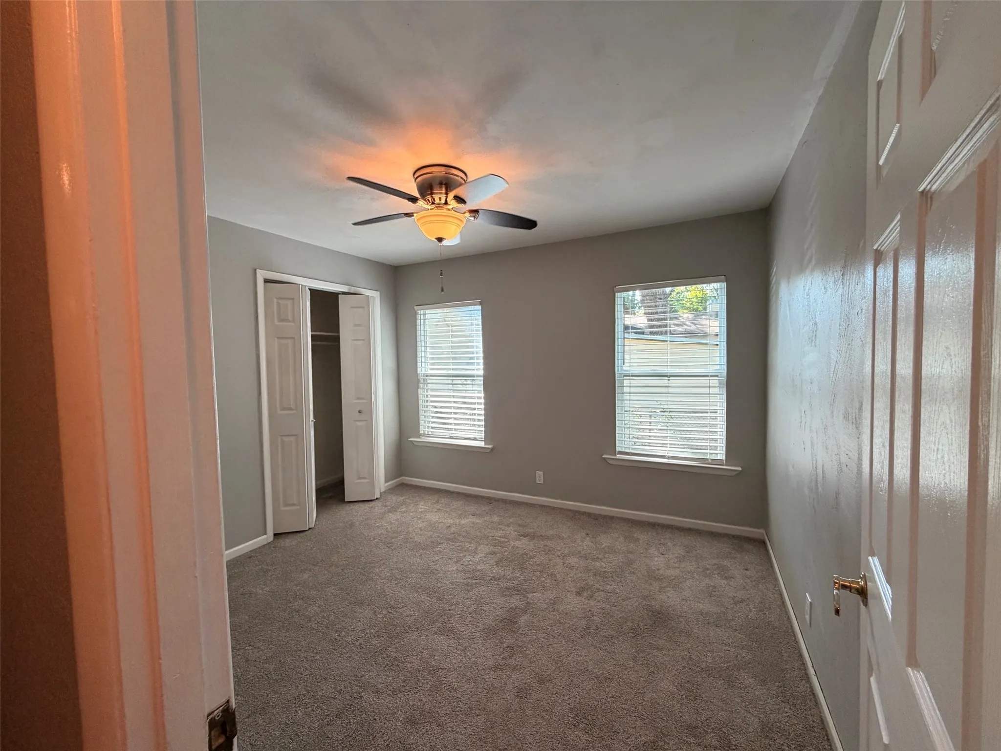 Recessed lighting with ceiling fan, two windows with blinds, carpeted flooring, and bi-fold closet doors