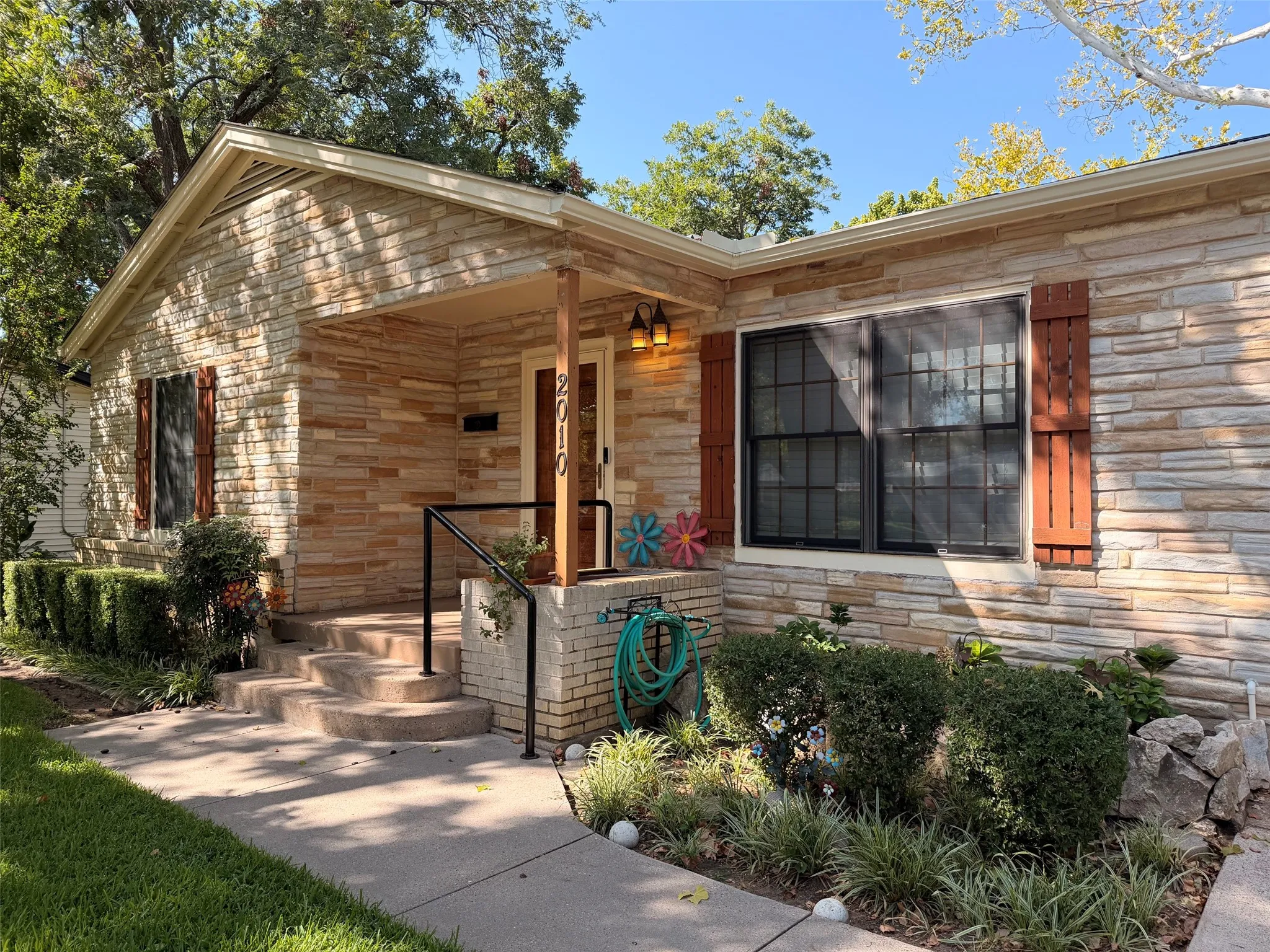 Stone veneer exterior with wood shutters, covered front porch, concrete steps, and established landscaping