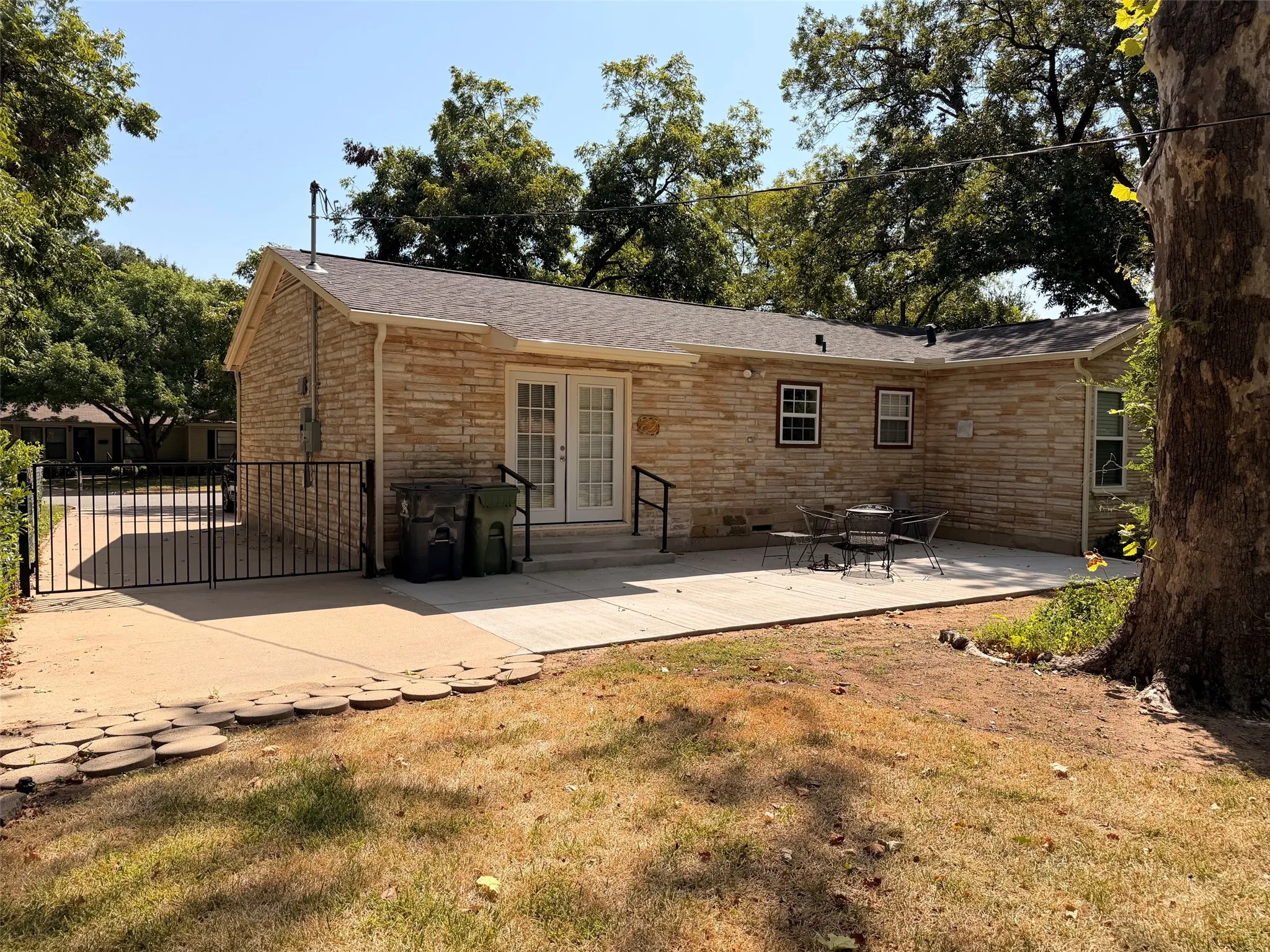 Stone exterior featuring a gabled roofline, concrete patio, and mature trees, gate to extra parking on the side