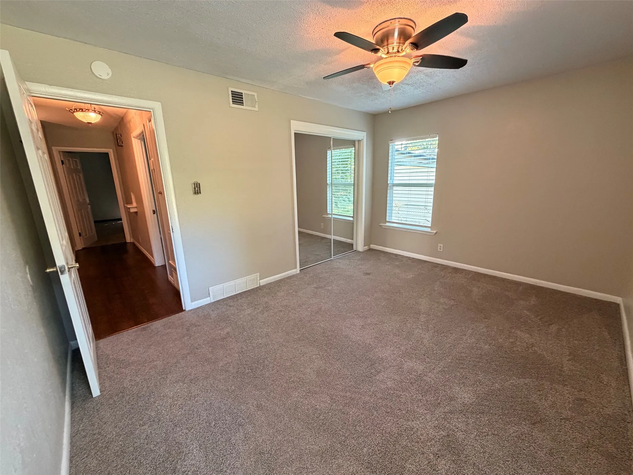 Carpeted flooring, ceiling fan, natural light from a window, mirrored closet doors, and neutral wall paint