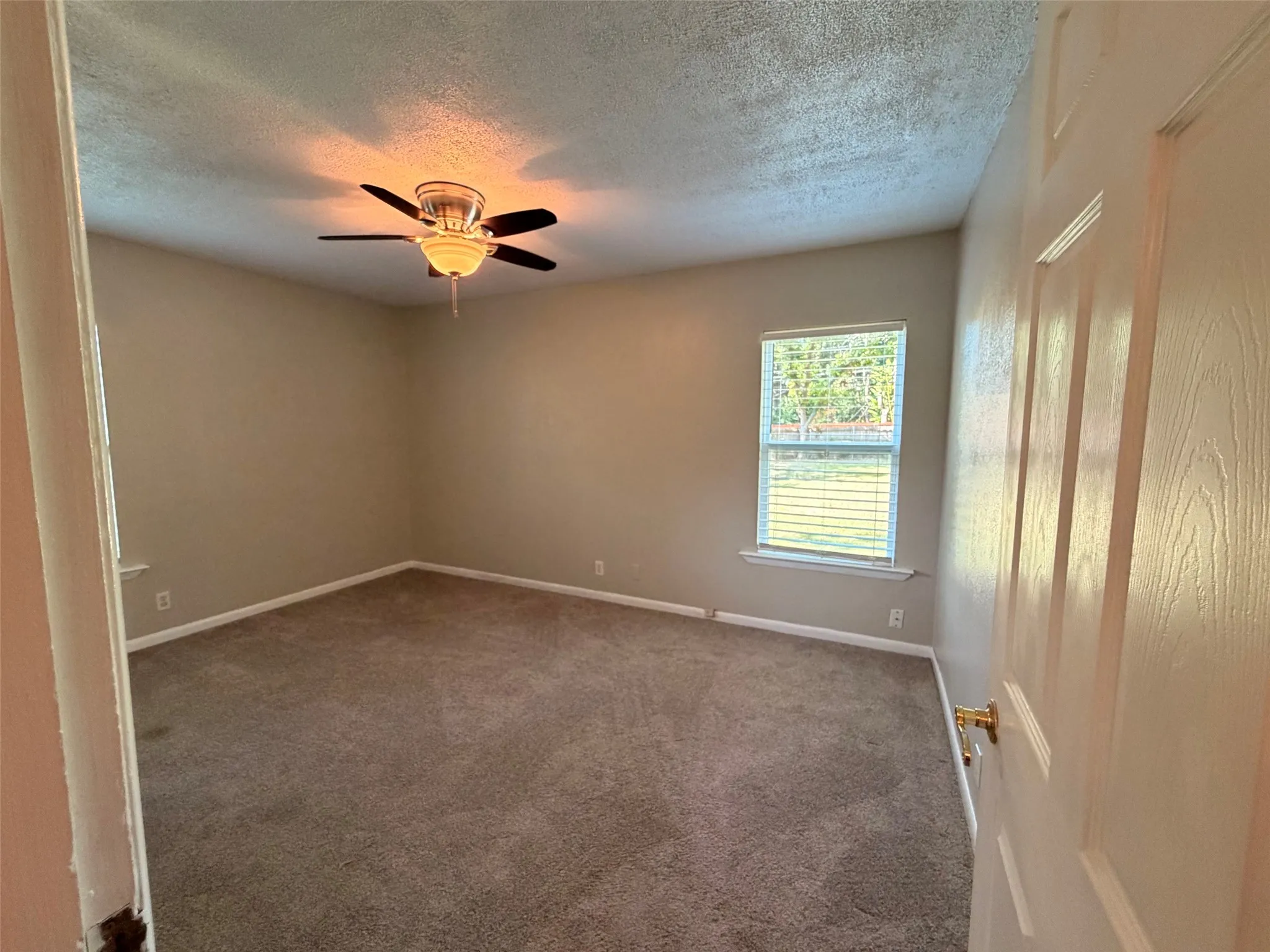 Carpeted interior space featuring a ceiling fan with integrated lighting and a window with blinds