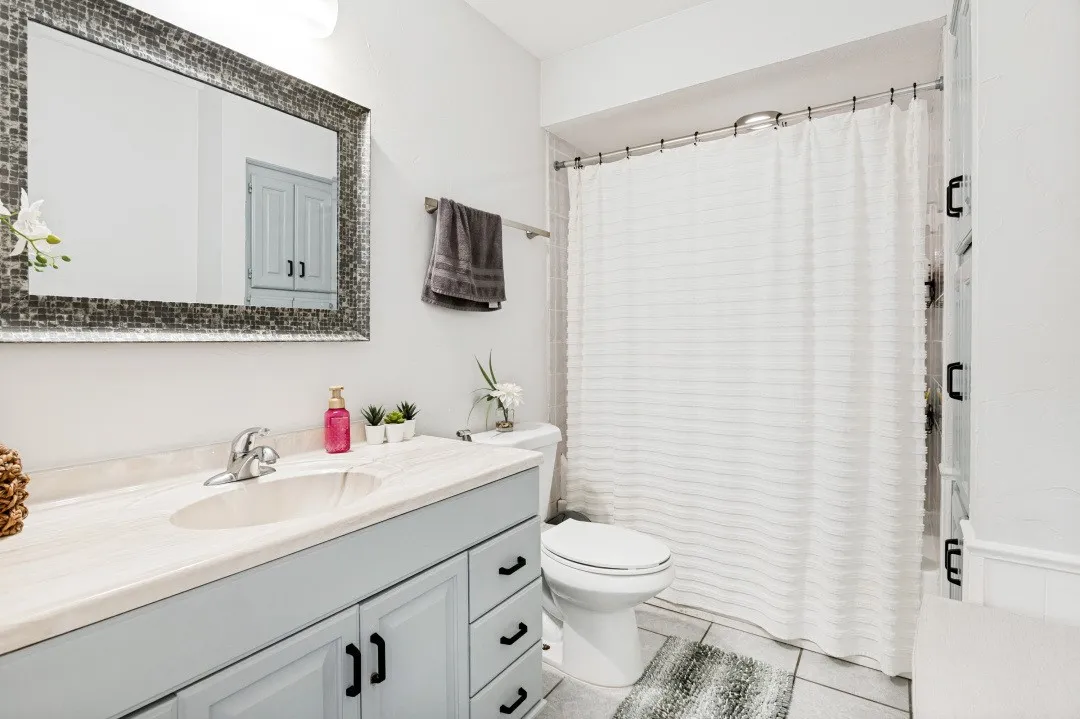 Vanity with an integrated sink and light-toned countertop, mosaic-framed mirror, and a white toilet