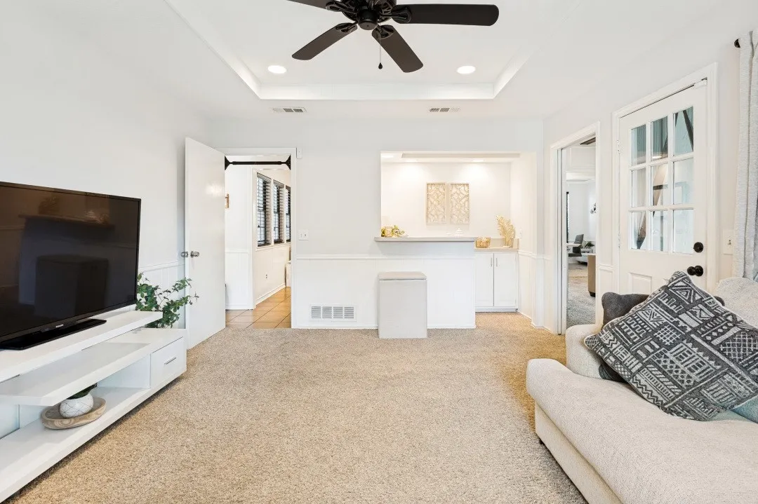 Recessed tray ceiling with a black ceiling fan, white paneled doors, and a built-in bar area with cabinetry and under-cabinet lighting