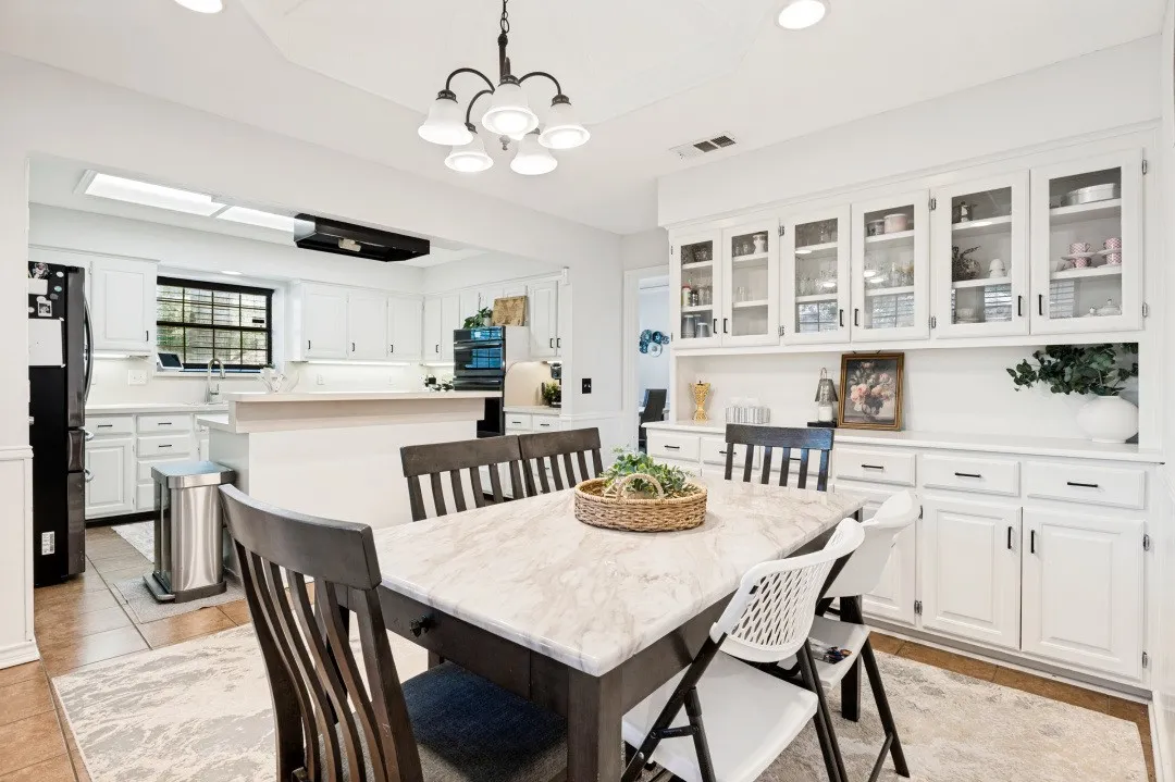 Kitchen and dining area featuring white cabinetry, a kitchen island, a skylight, and built-in glass-front upper cabinets