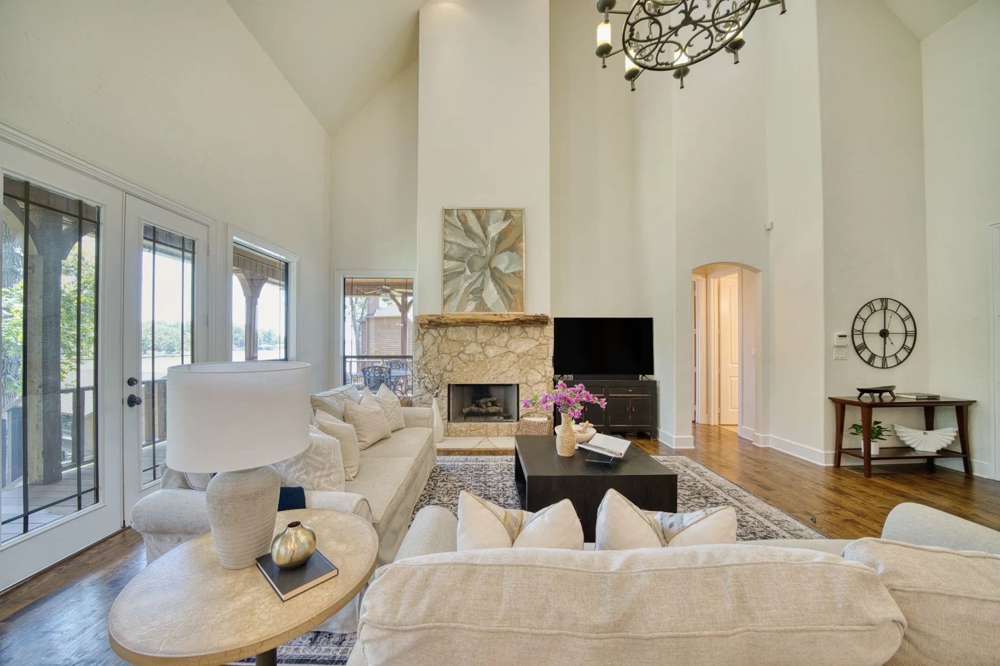 Vaulted ceilings, a stone fireplace, wood-finish flooring, and French doors with transoms