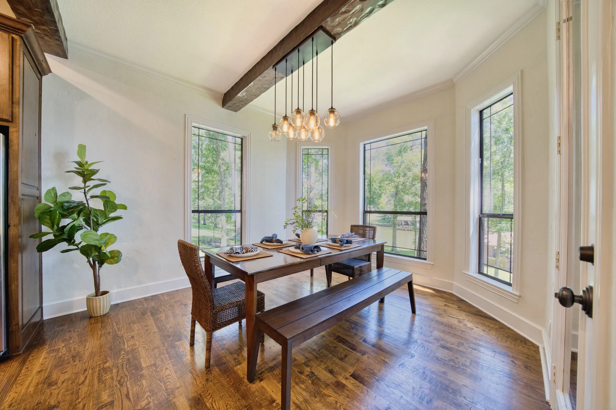 Dining area featuring wood-finish flooring, exposed ceiling beams, a multi-bulb chandelier, and multiple tall windows