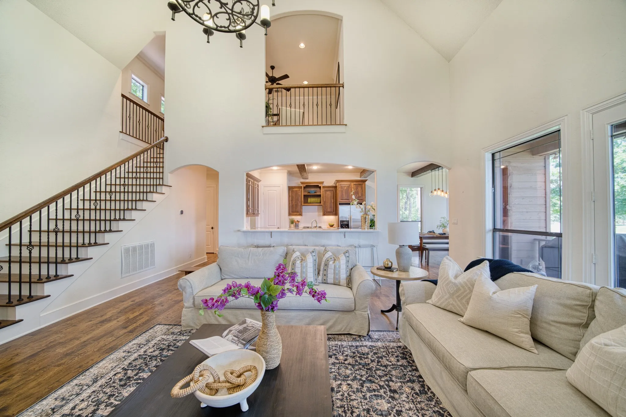 Vaulted ceiling, wood-finish flooring, wrought iron staircase railing, arched doorways, and upper-level balcony