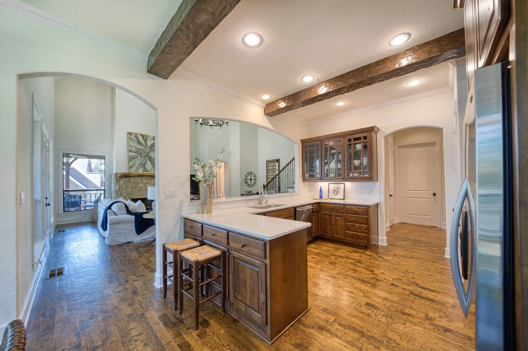 Wood-finish flooring, exposed ceiling beams, recessed lighting, wood cabinetry, and a stainless steel refrigerator