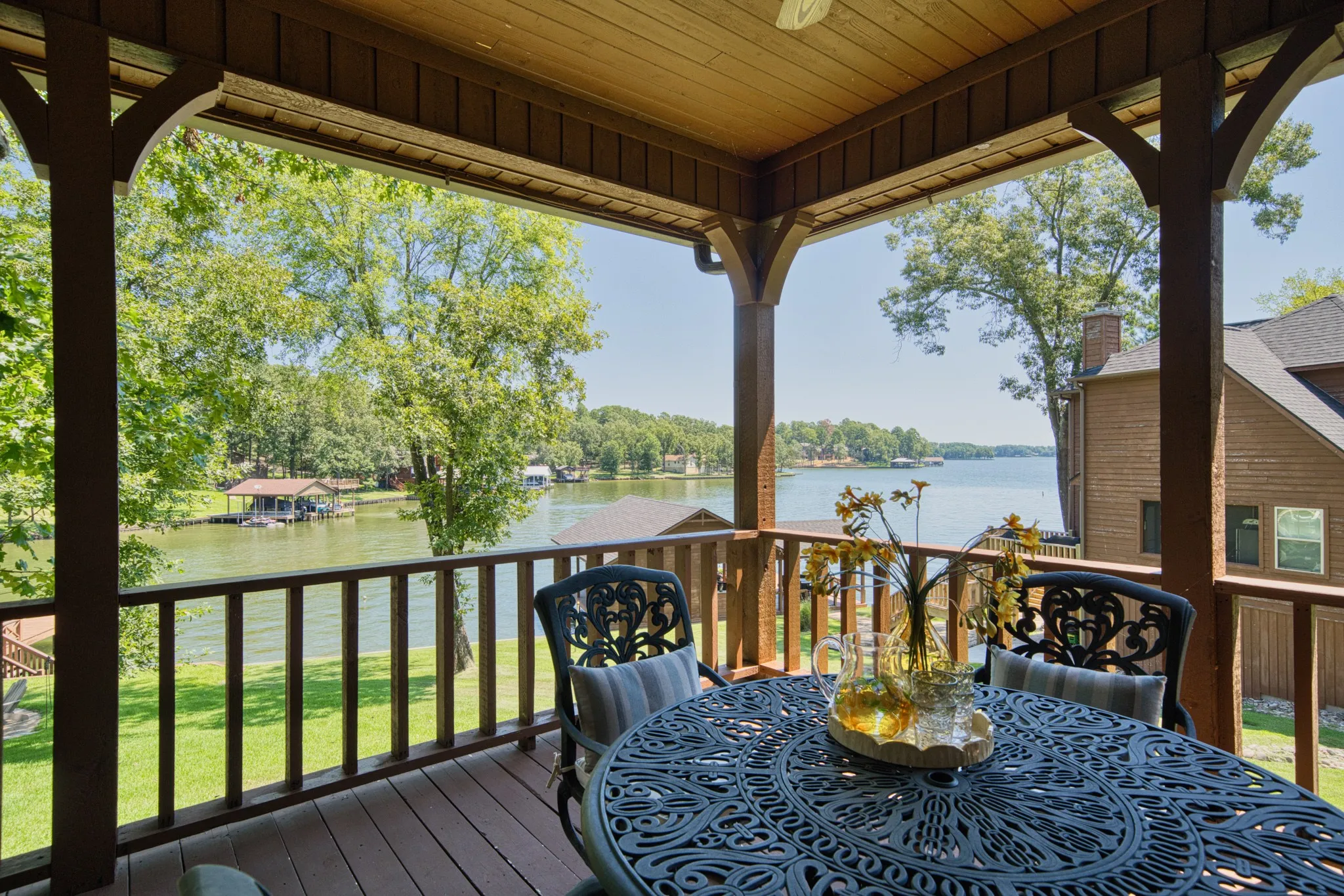 Covered wooden deck with lake frontage, wood-finish flooring, and architectural columns