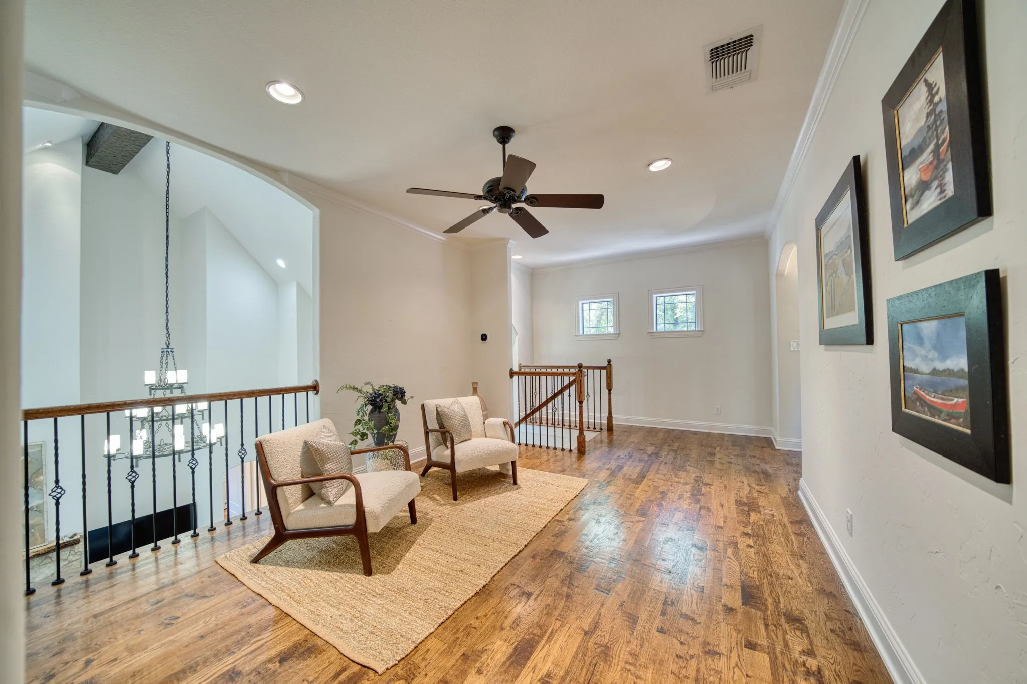 Wood-finish flooring, recessed lighting, and a ceiling fan are featured in this space with a wrought iron and wood railing