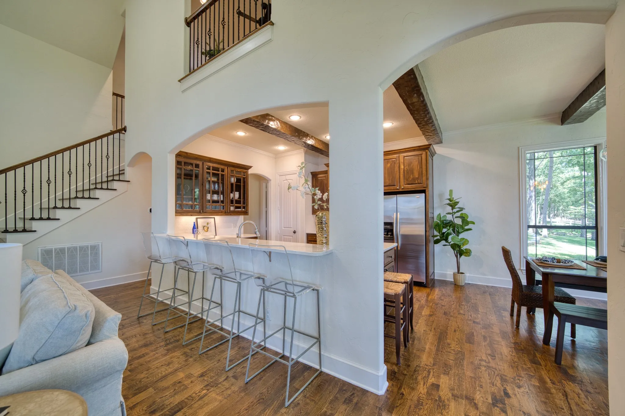 Two-story ceiling, wood-finish flooring, staircase with wrought iron balusters, arched doorways, and a breakfast bar with stone countertop