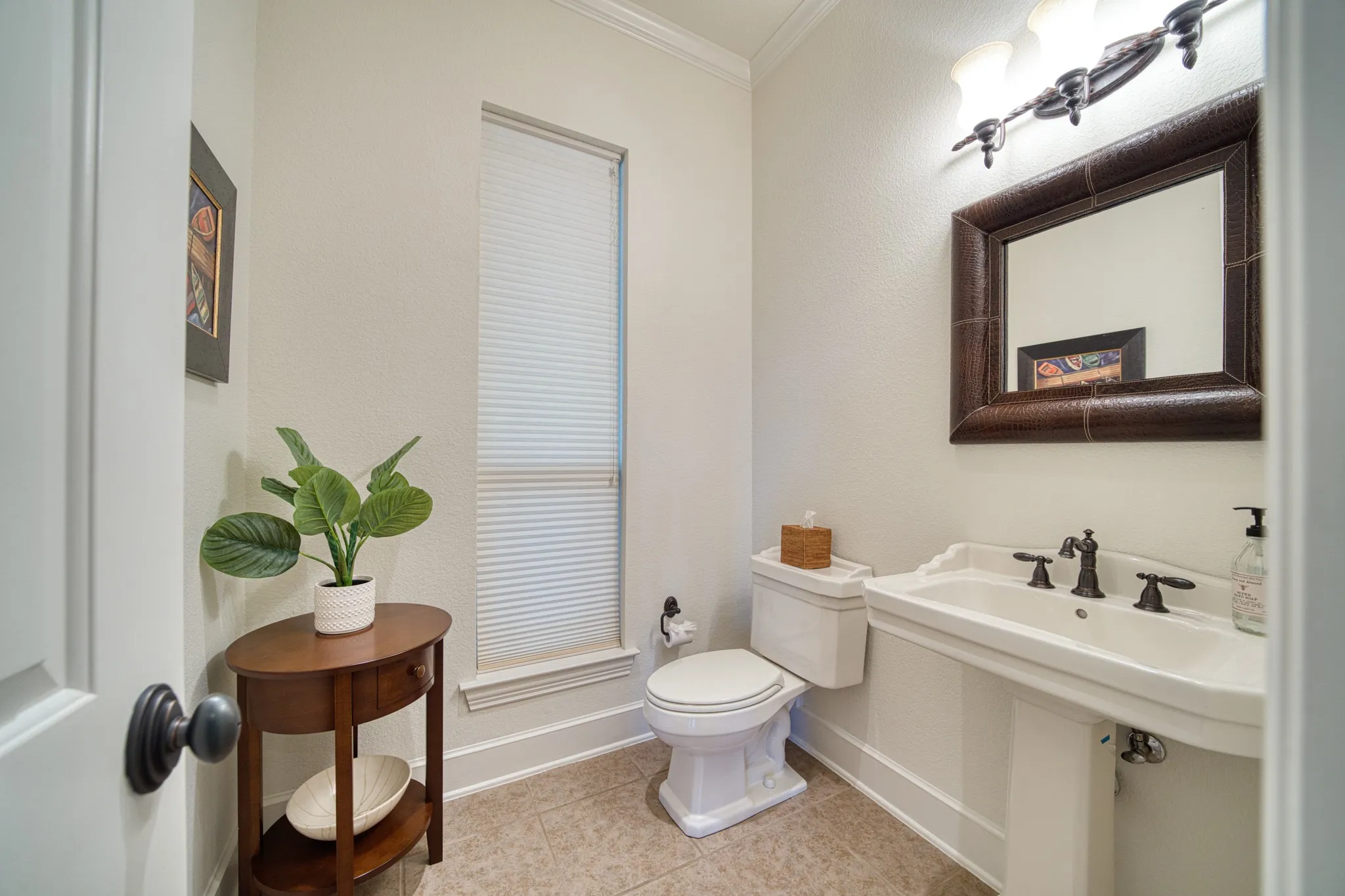 Pedestal sink with dark bronze fixtures, framed mirror, and crown molding