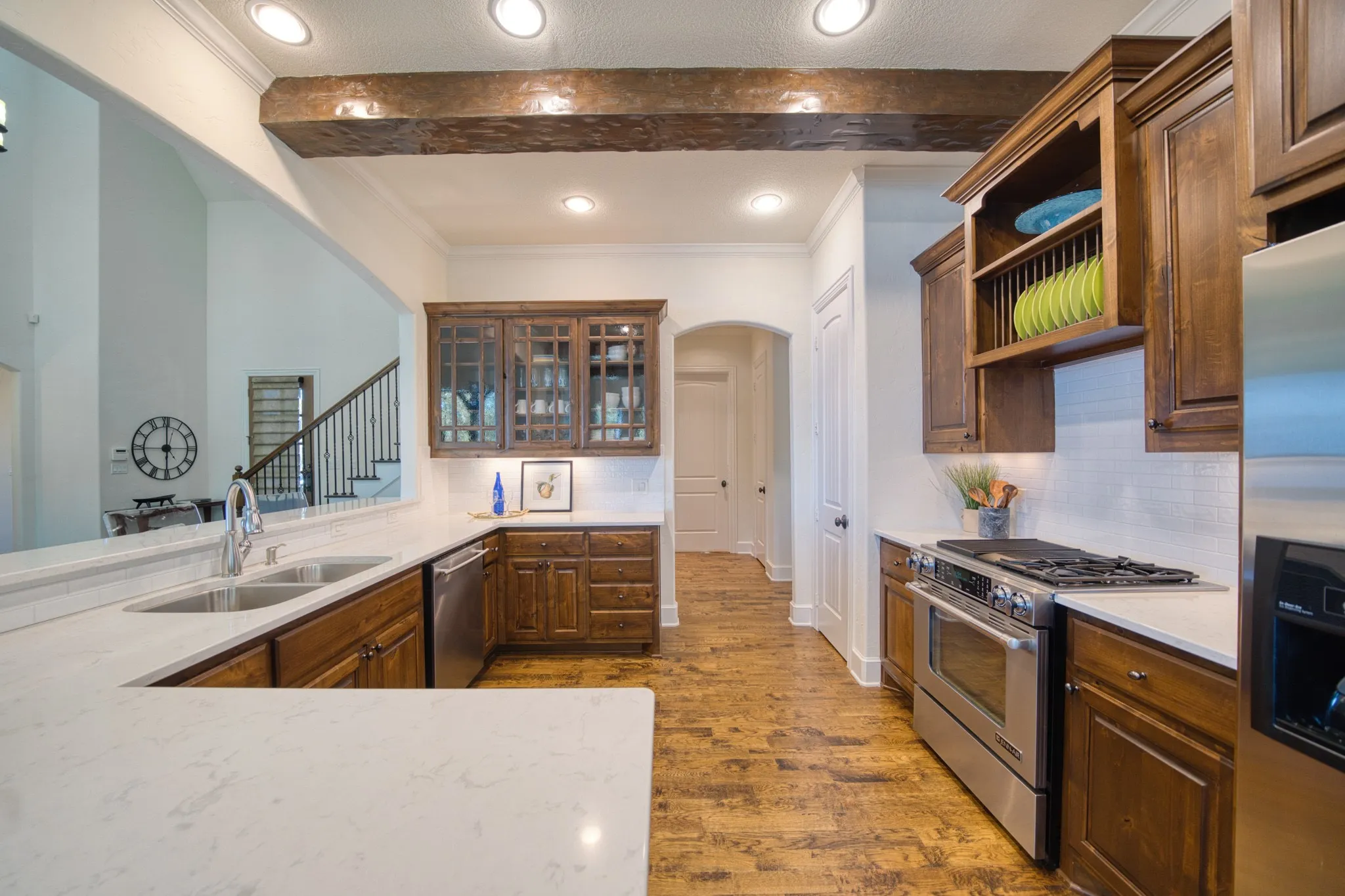 U-shaped kitchen featuring wood-finish flooring, white countertops, dark wood cabinetry, stainless steel appliances, and a white subway tile backsplash