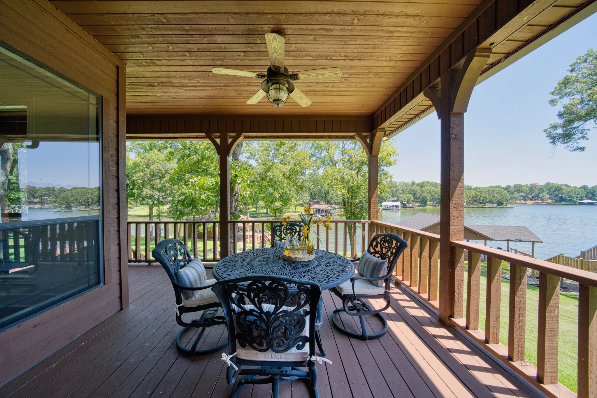 Expansive covered deck featuring a wood plank ceiling, an outdoor ceiling fan, and a wood-finish railing overlooking a body of water