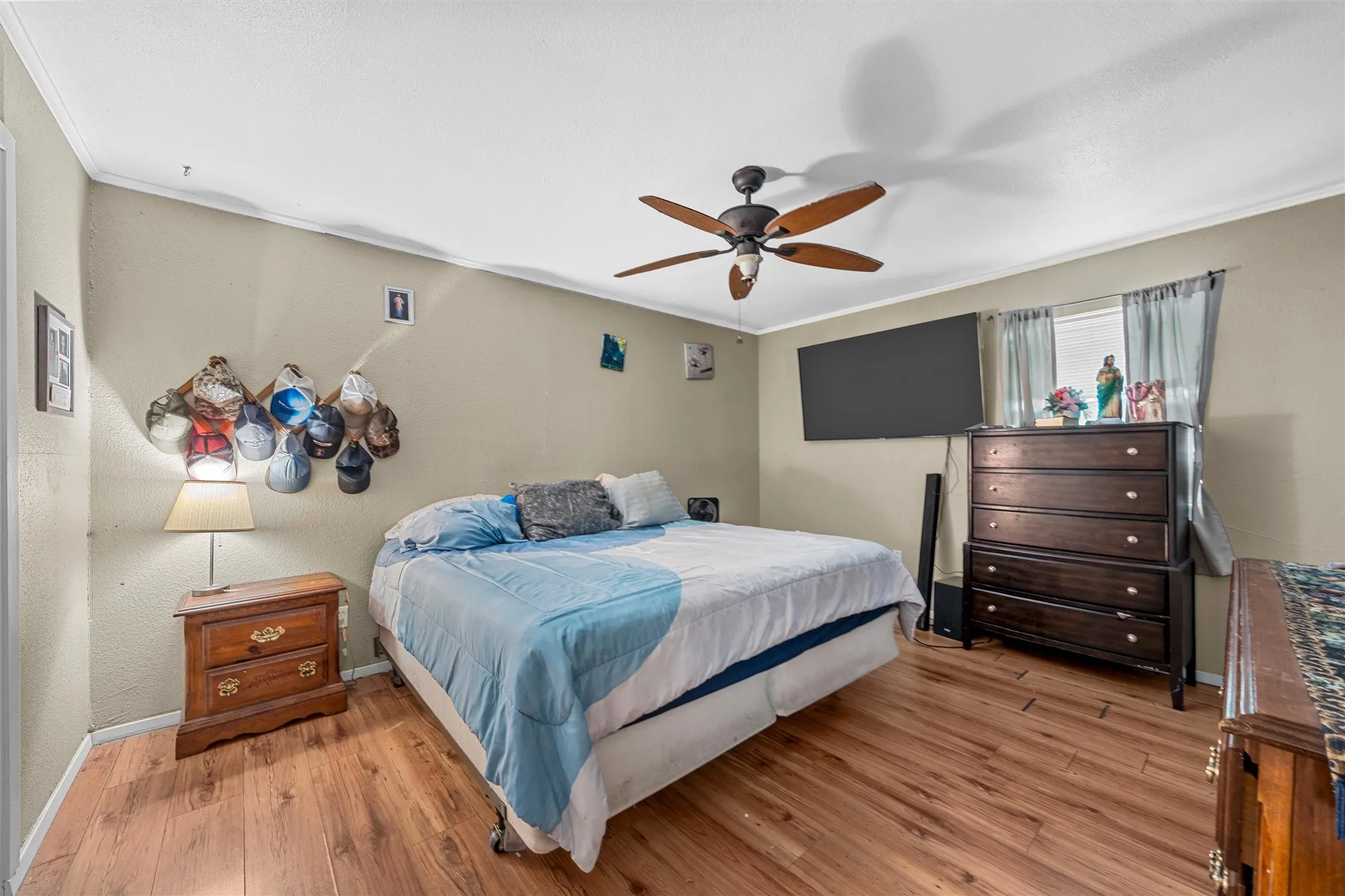 Wood-finish flooring throughout, ceiling fan with integrated lighting, window with drapes, and neutral wall paint