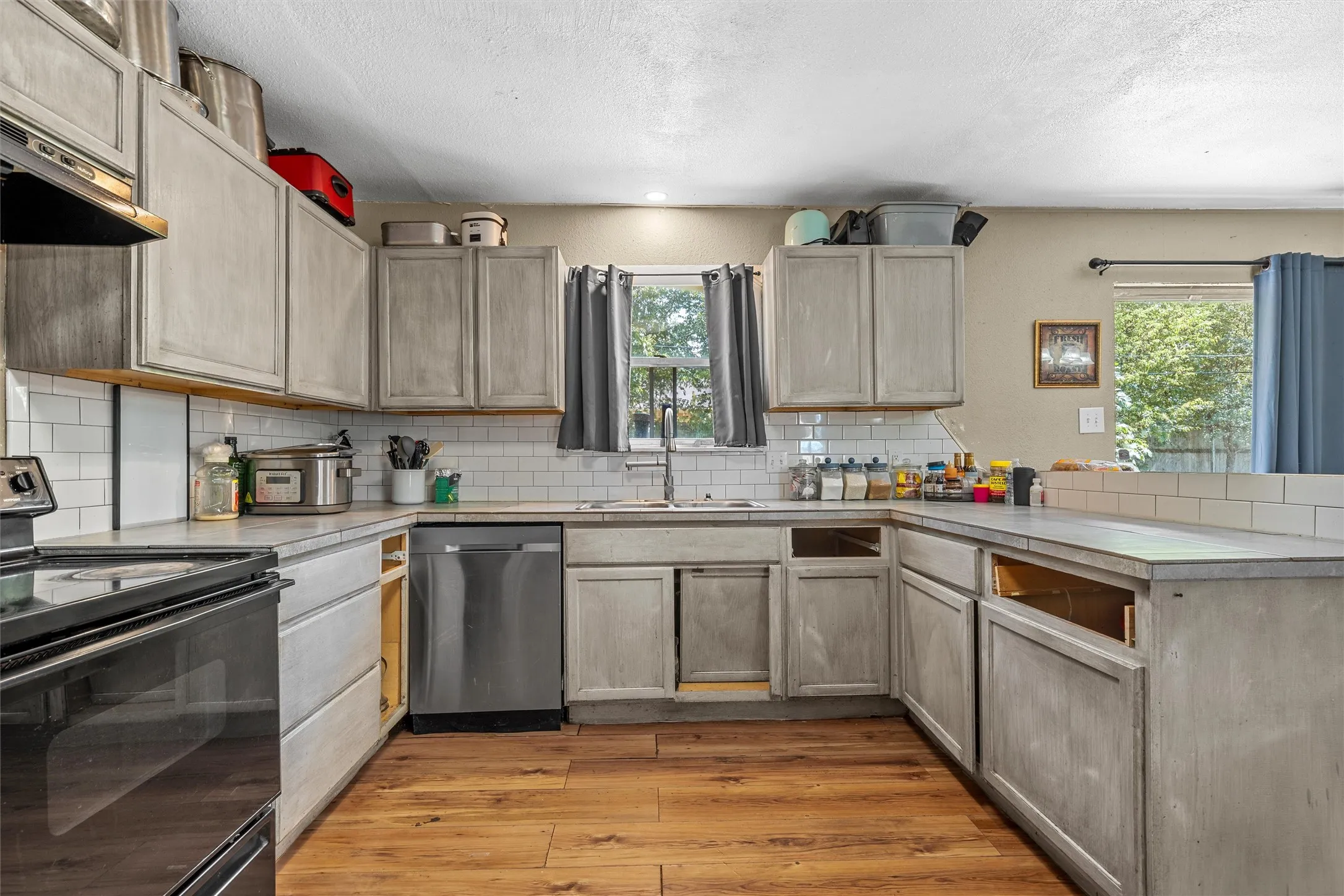 U-shaped kitchen layout with wood-finish flooring, subway tile backsplash, and a stainless steel dishwasher