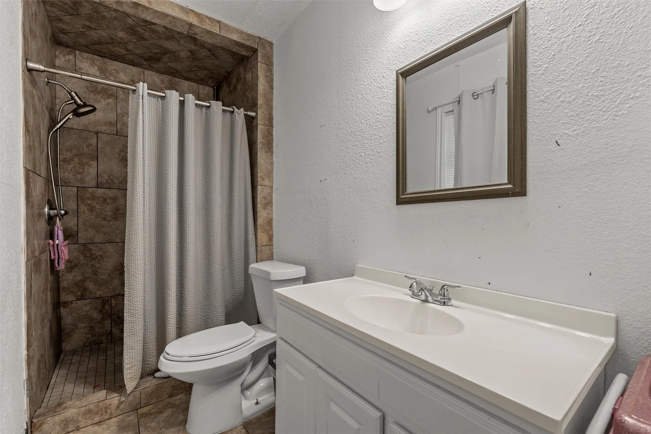 Tiled shower stall with an adjustable shower head, white vanity with an integrated sink, and a framed mirror