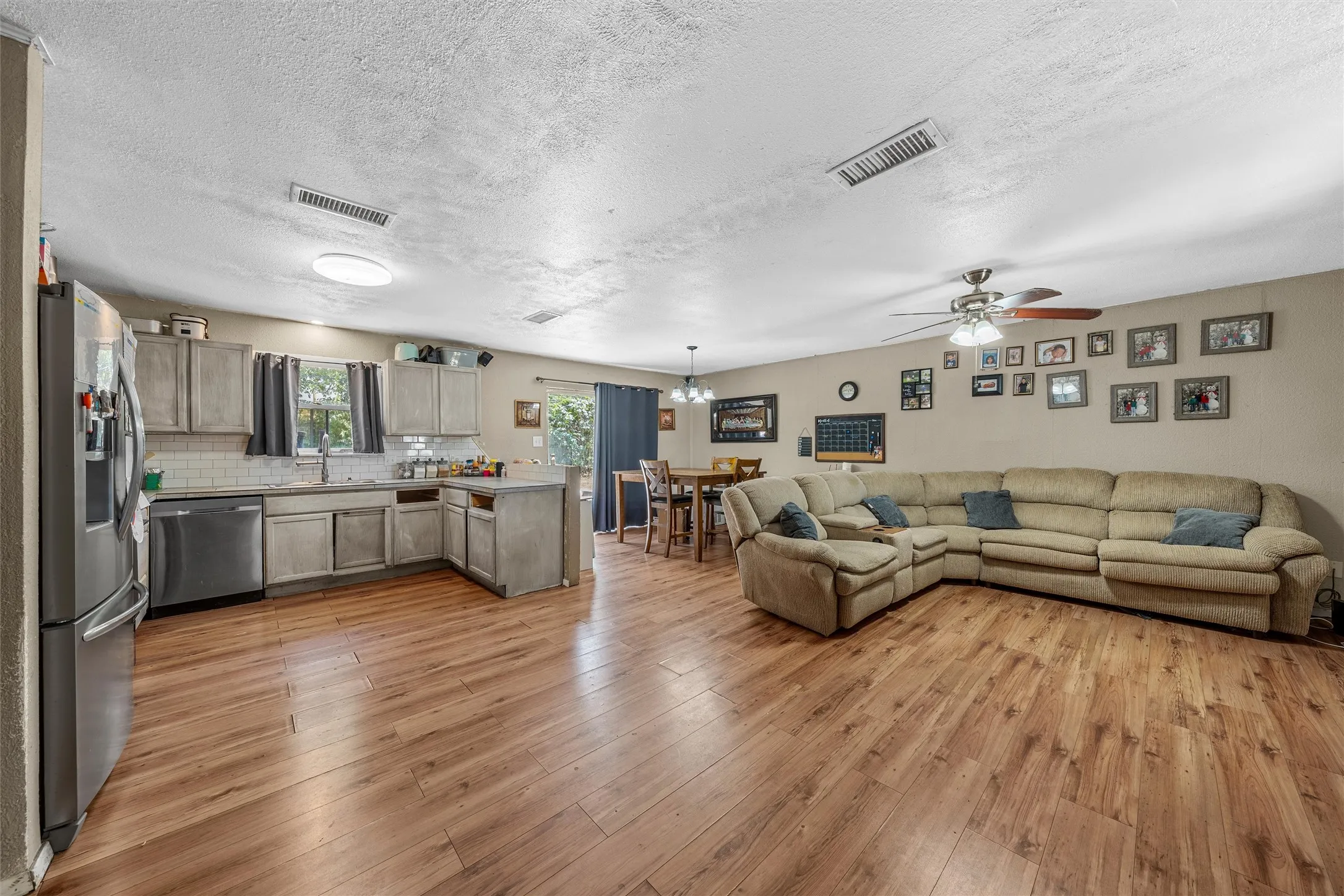 Open-concept living area featuring wood-finish flooring, a ceiling fan, a kitchen island, grey cabinetry, and stainless steel appliances