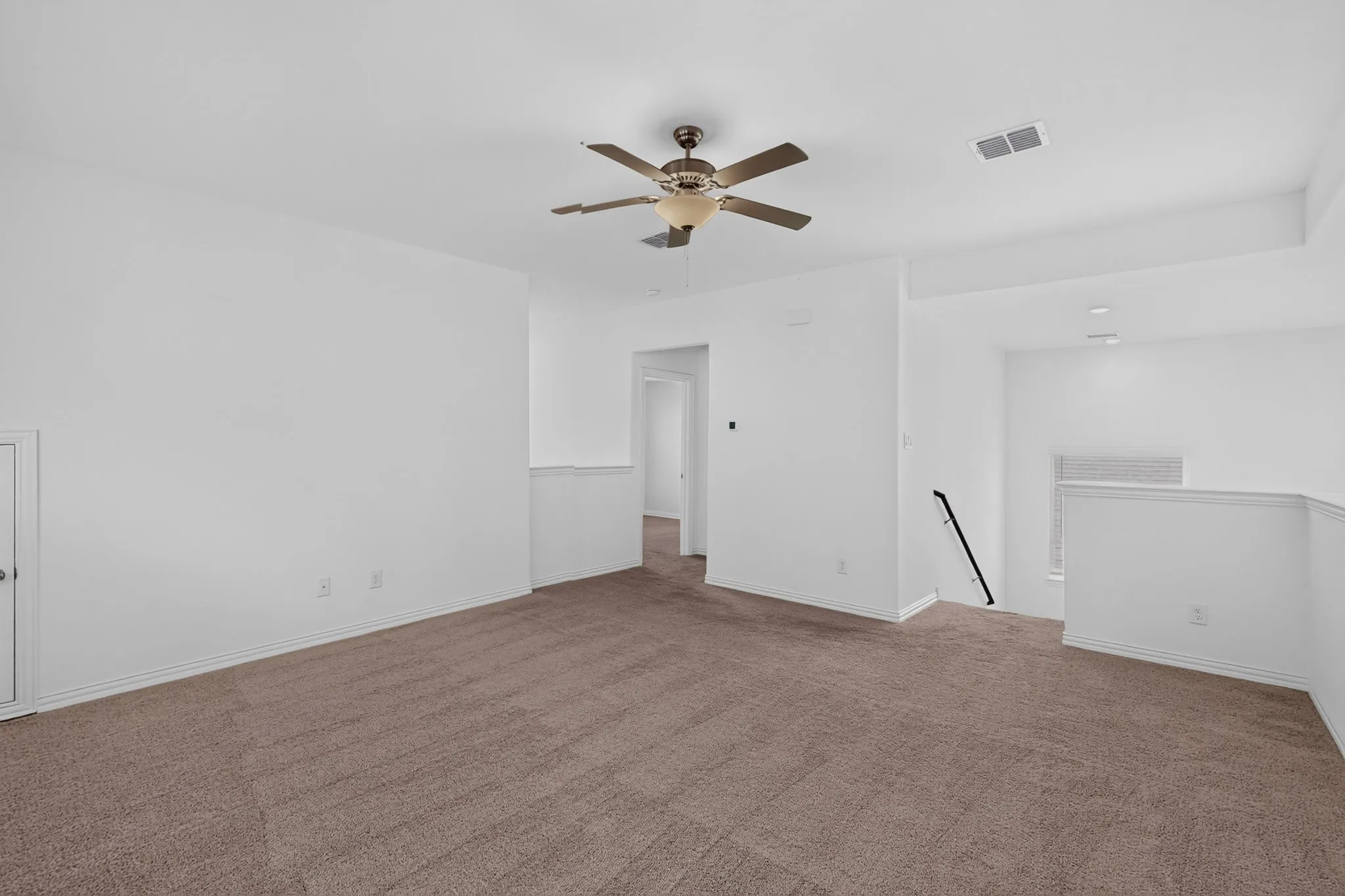 Carpeted room featuring a ceiling fan, tray ceiling, and a partial wall with a handrail
