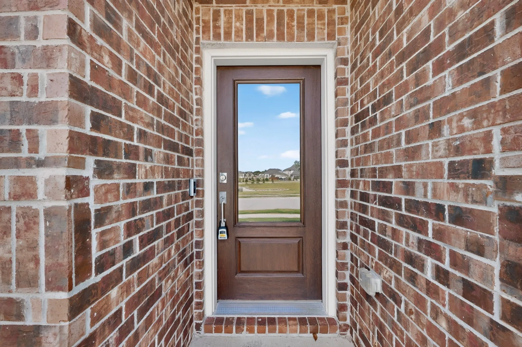 Brick exterior featuring a wood-finish entry door with glass insert and white trim