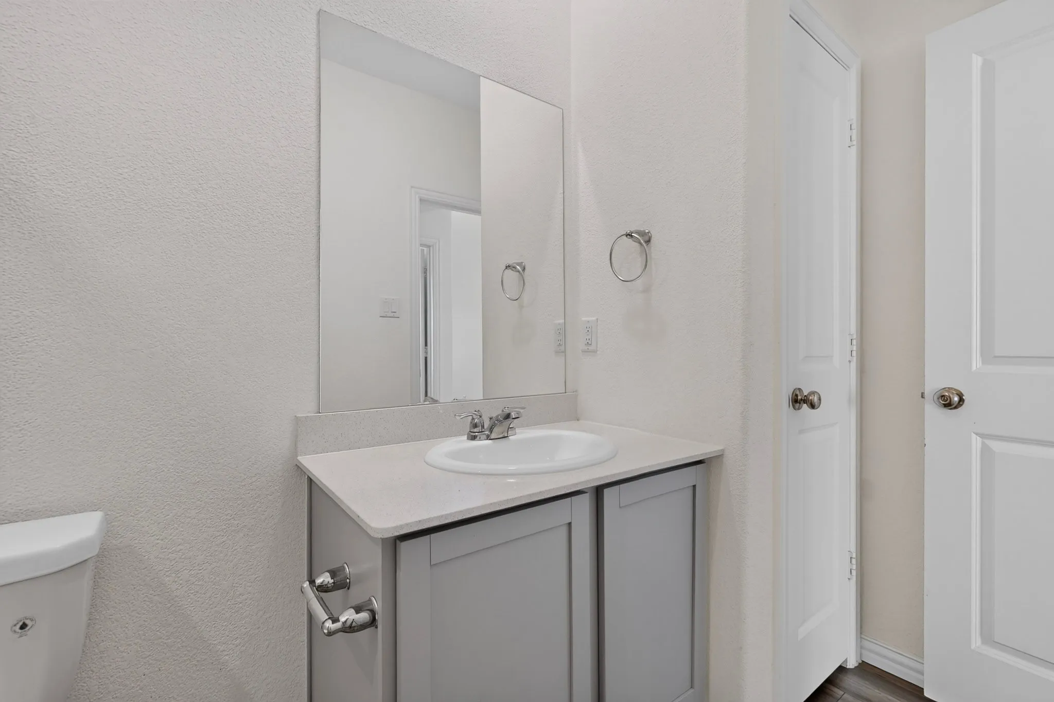 Vanity with integrated sink, chrome faucet, and gray cabinetry, complemented by a large wall-mounted mirror