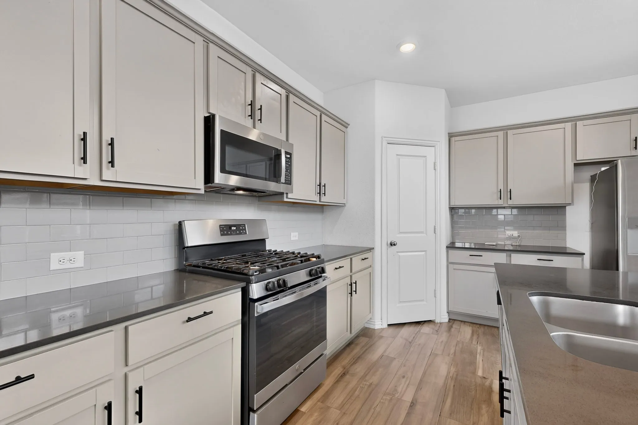 Gray shaker cabinetry, subway tile backsplash, stainless steel appliances, wood-finish flooring, and a stainless steel sink