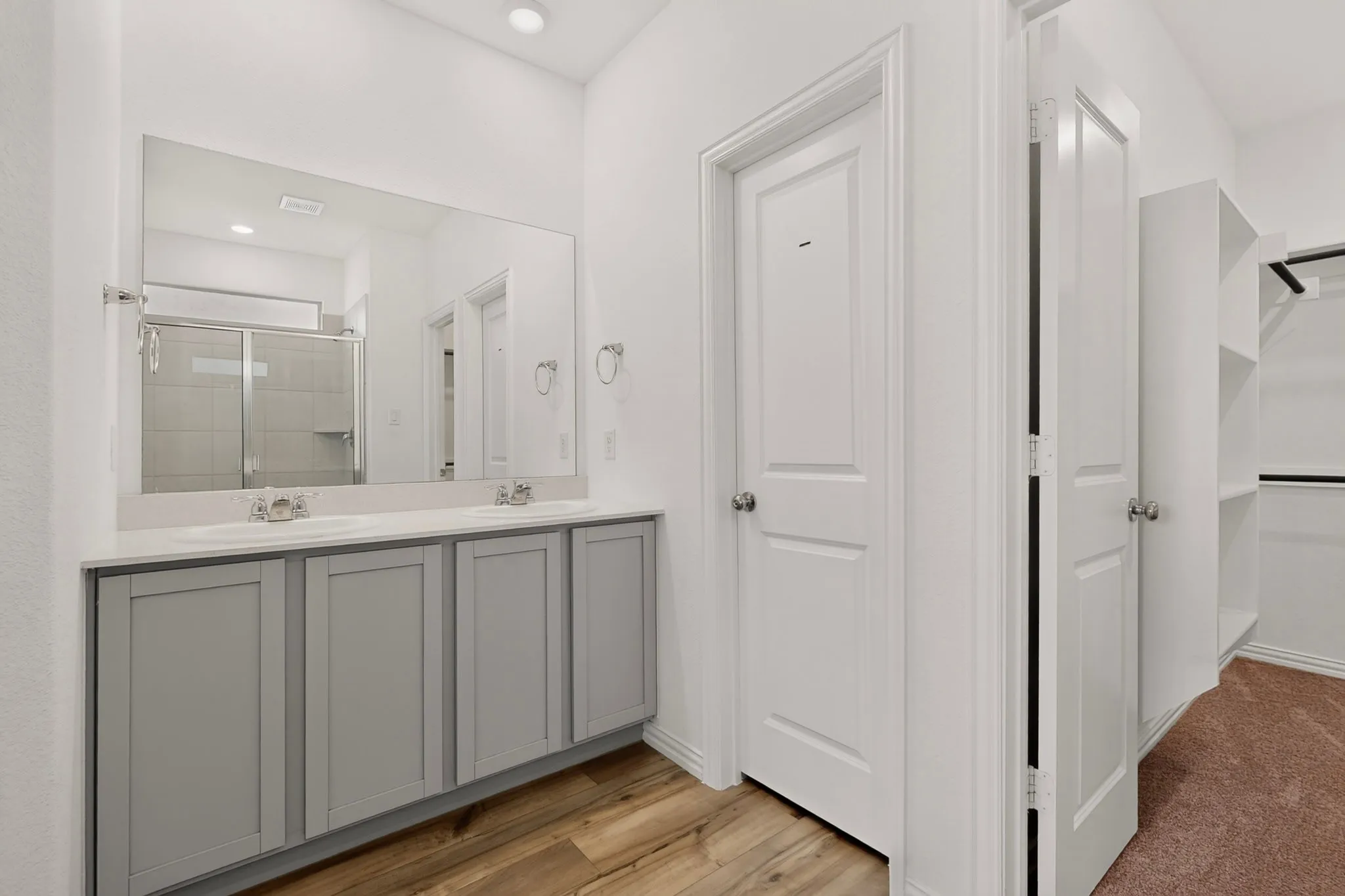 Double vanity with undermount sinks, wood-finish flooring, recessed lighting, and a walk-in shower with sliding glass doors