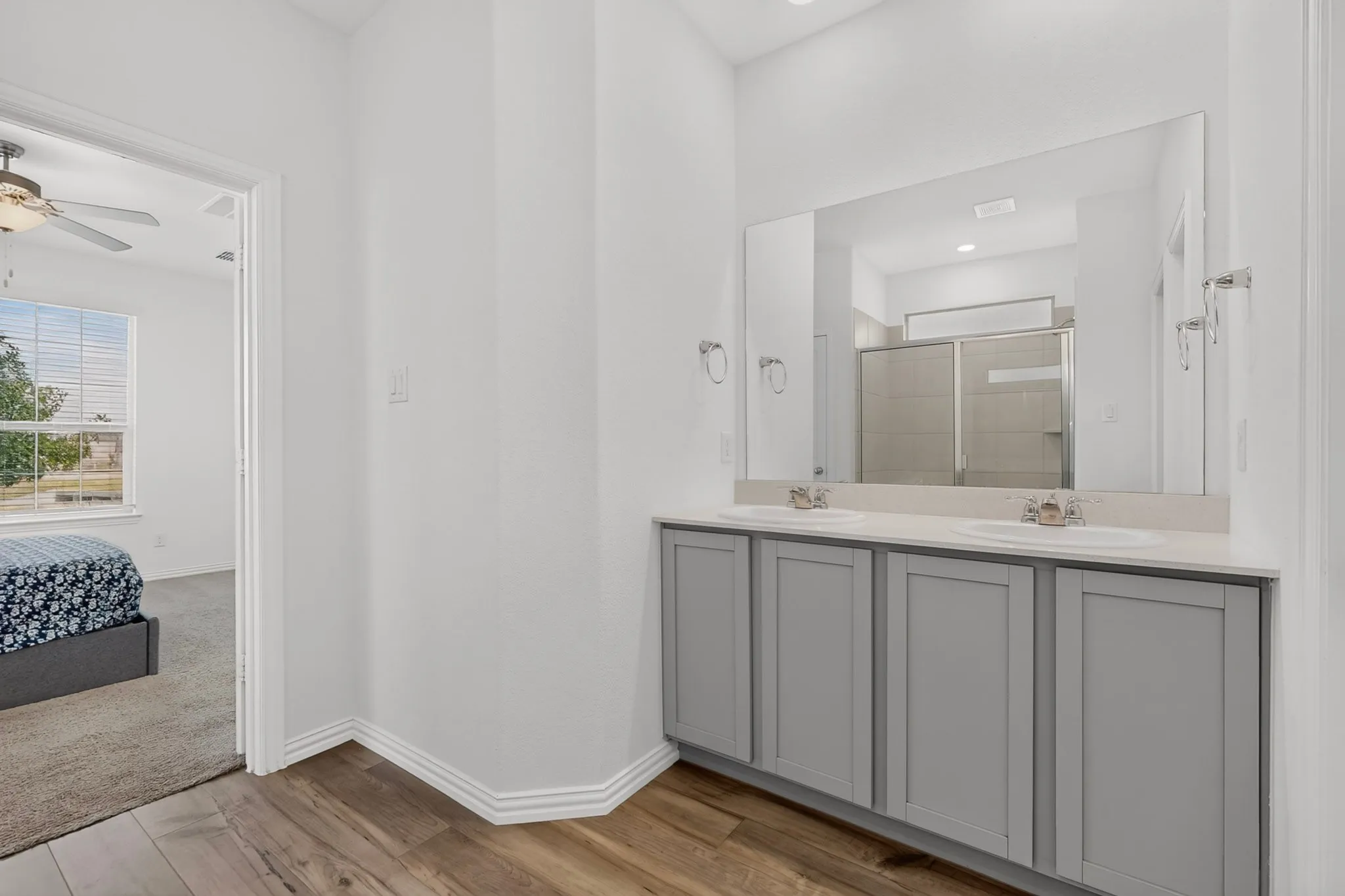 Dual vanity with gray cabinetry and undermount sinks, illuminated by recessed lighting, with wood-finish flooring