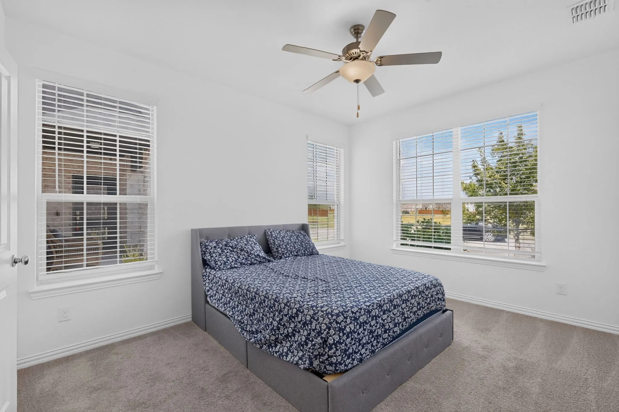 Neutral tone paint throughout, carpeted flooring, two large windows with blinds, and a ceiling fan with integrated lighting