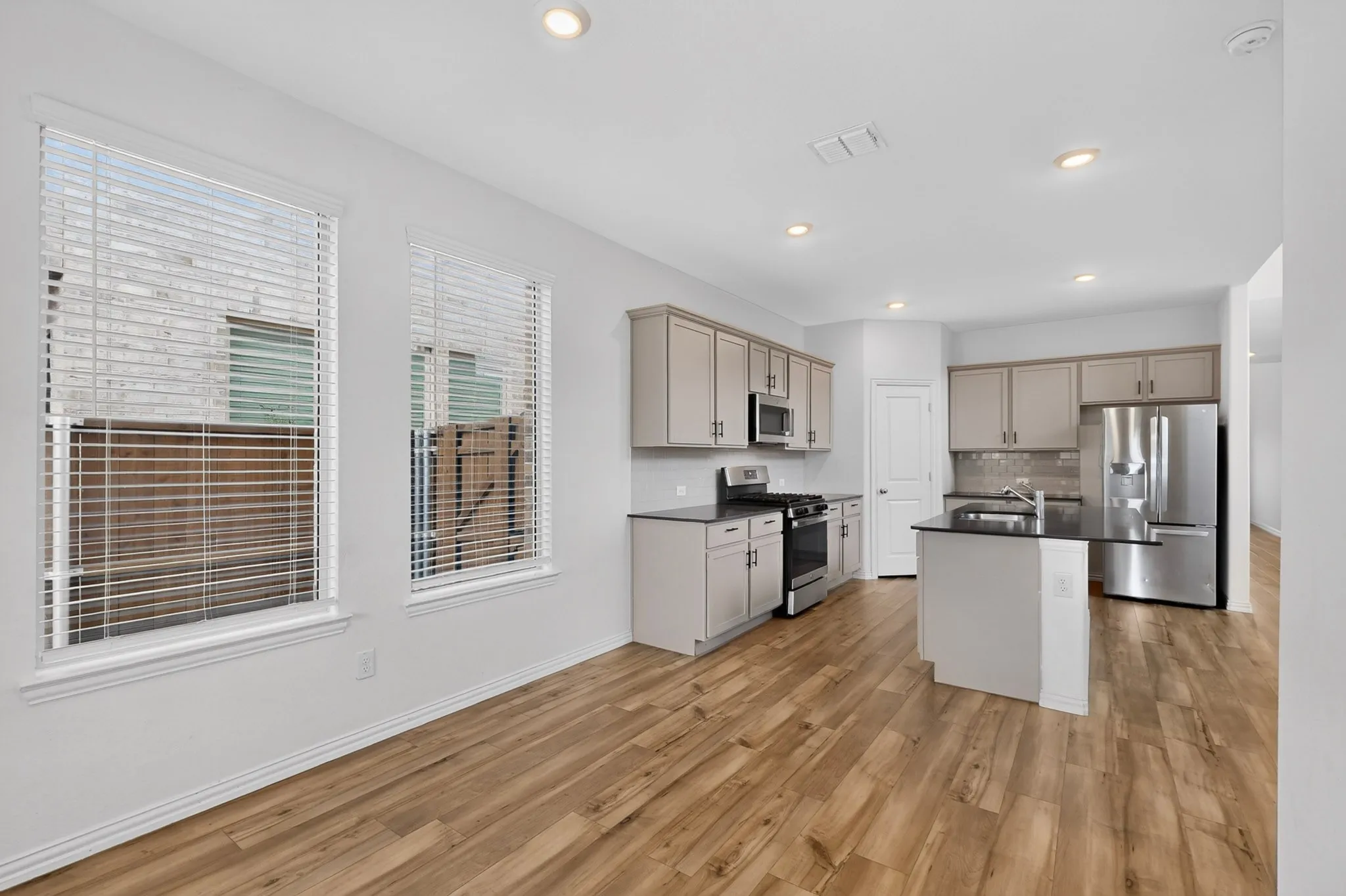 Open-concept kitchen featuring wood-finish flooring, recessed lighting, a kitchen island with dark countertop, stainless steel appliances, and neutral cabinetry