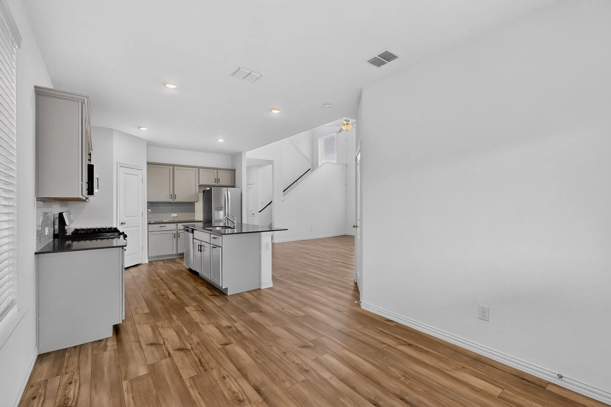 Open-concept living area with wood-finish flooring, a kitchen island with seating, stainless steel appliances, and recessed lighting