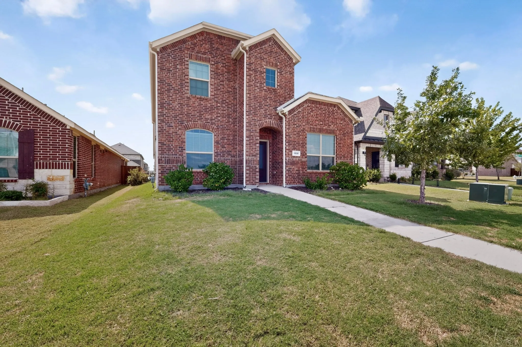 Striking two-story brick residence featuring a peaked roofline with architectural gables, multiple windows allowing abundant natural light, and a manicured lawn with mature landscaping