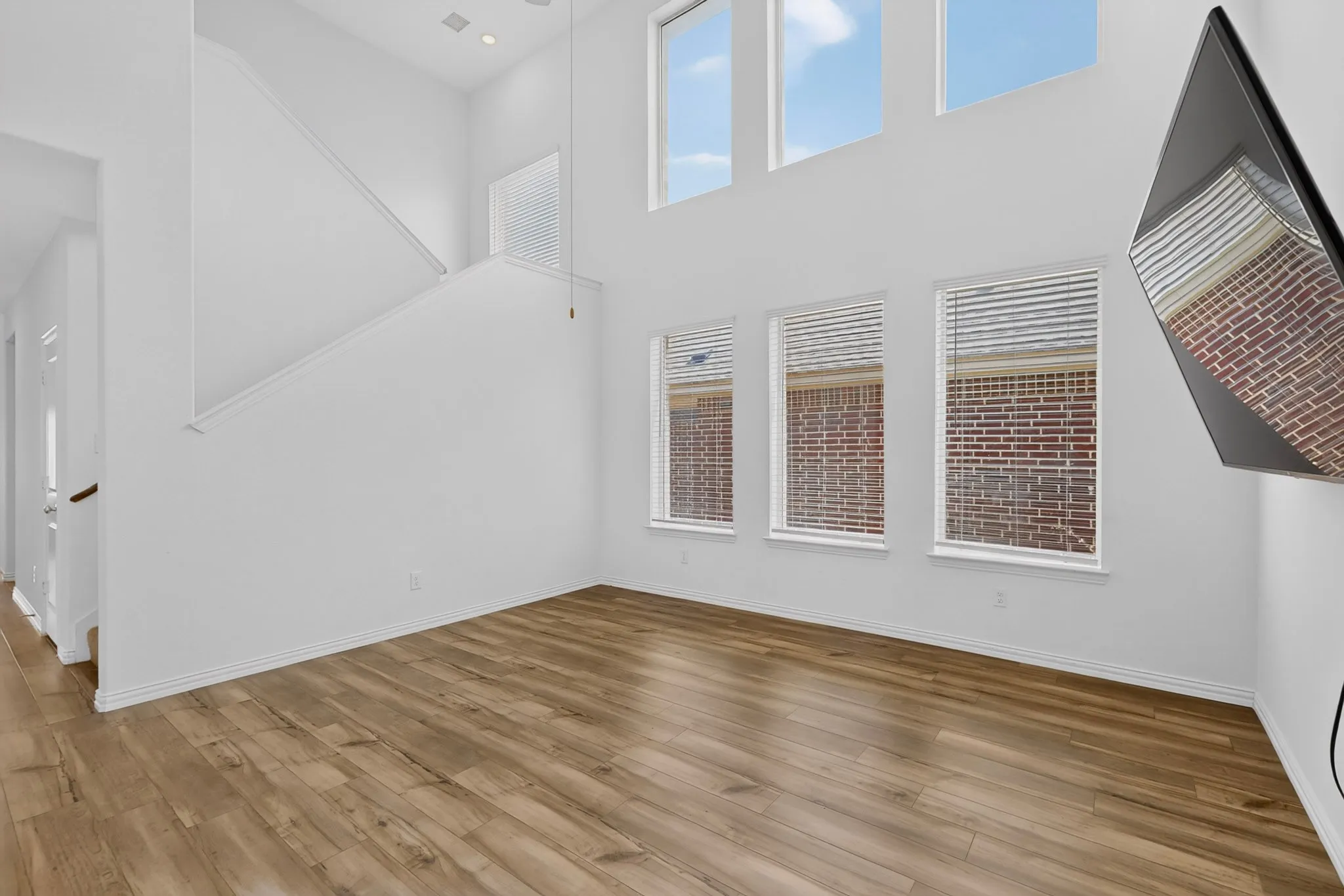 Soaring ceiling, wood-finish flooring, white walls, and multiple windows