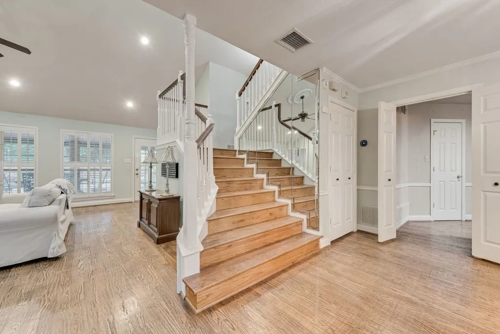 Hardwood flooring throughout, a grand staircase with wood newel posts and white balusters, recessed lighting, and multiple windows with plantation shutters