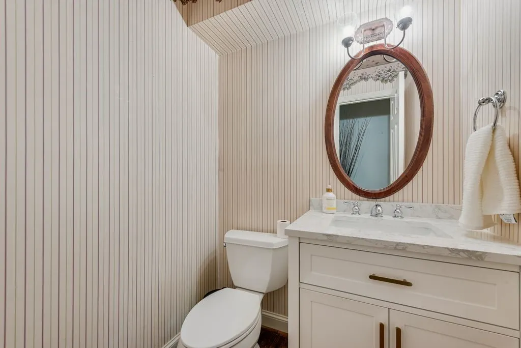 White vanity with a stone countertop, an oval wood-framed mirror, and a chrome towel ring