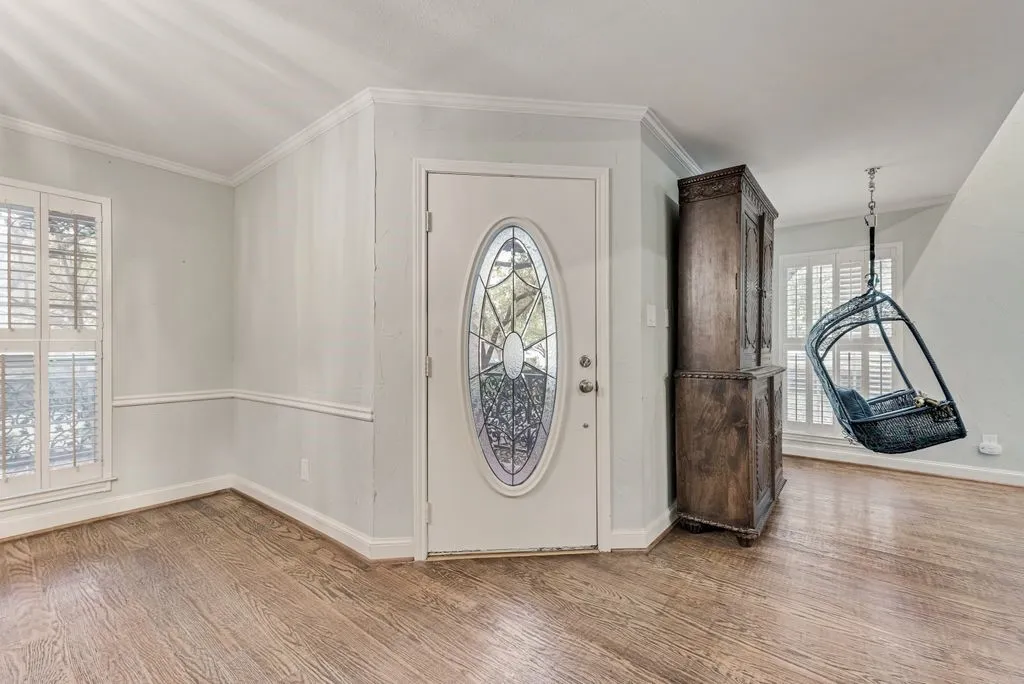 Entryway featuring wood-finish flooring, a front door with an oval stained-glass insert, and white plantation shutters