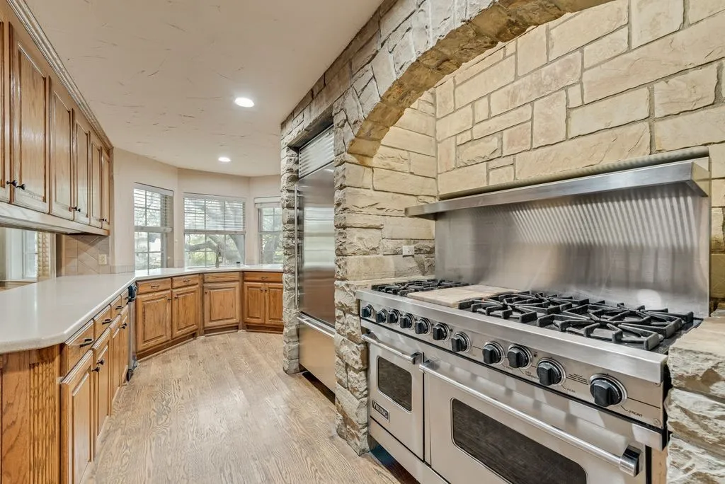 Gourmet kitchen featuring a stainless steel range with griddle, stone archway, built-in stainless steel refrigerator, wood-finish flooring, and ample cabinetry