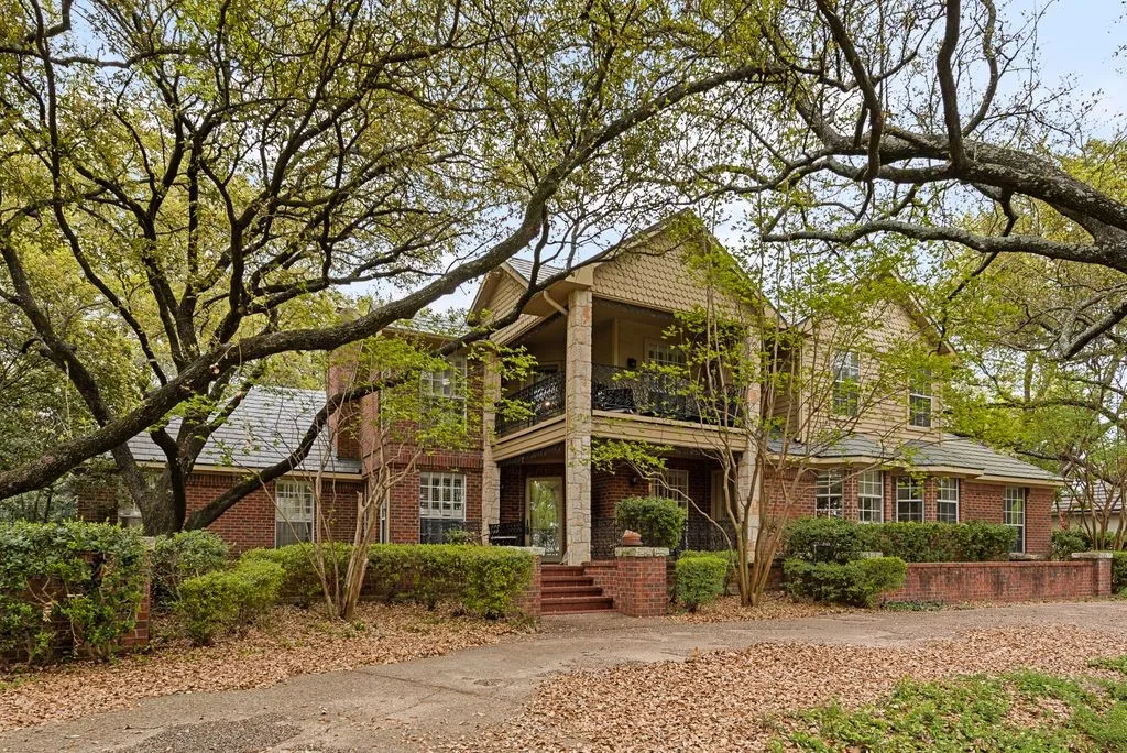 Brick exterior with a stone column porch, an upper-level balcony, dormer windows, and a multi-level roofline