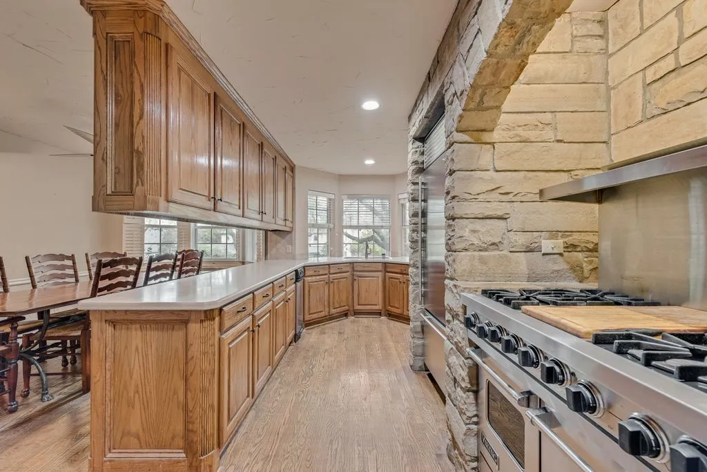 Stone archway with built-in range, stainless steel appliances, extensive wood cabinetry, light-toned countertops, and wood-finish flooring