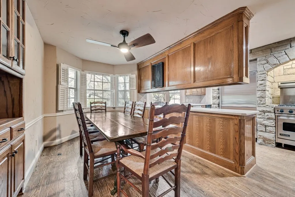Wood-finish flooring, bay windows with plantation shutters, wood paneling, stone archway, and stainless steel range