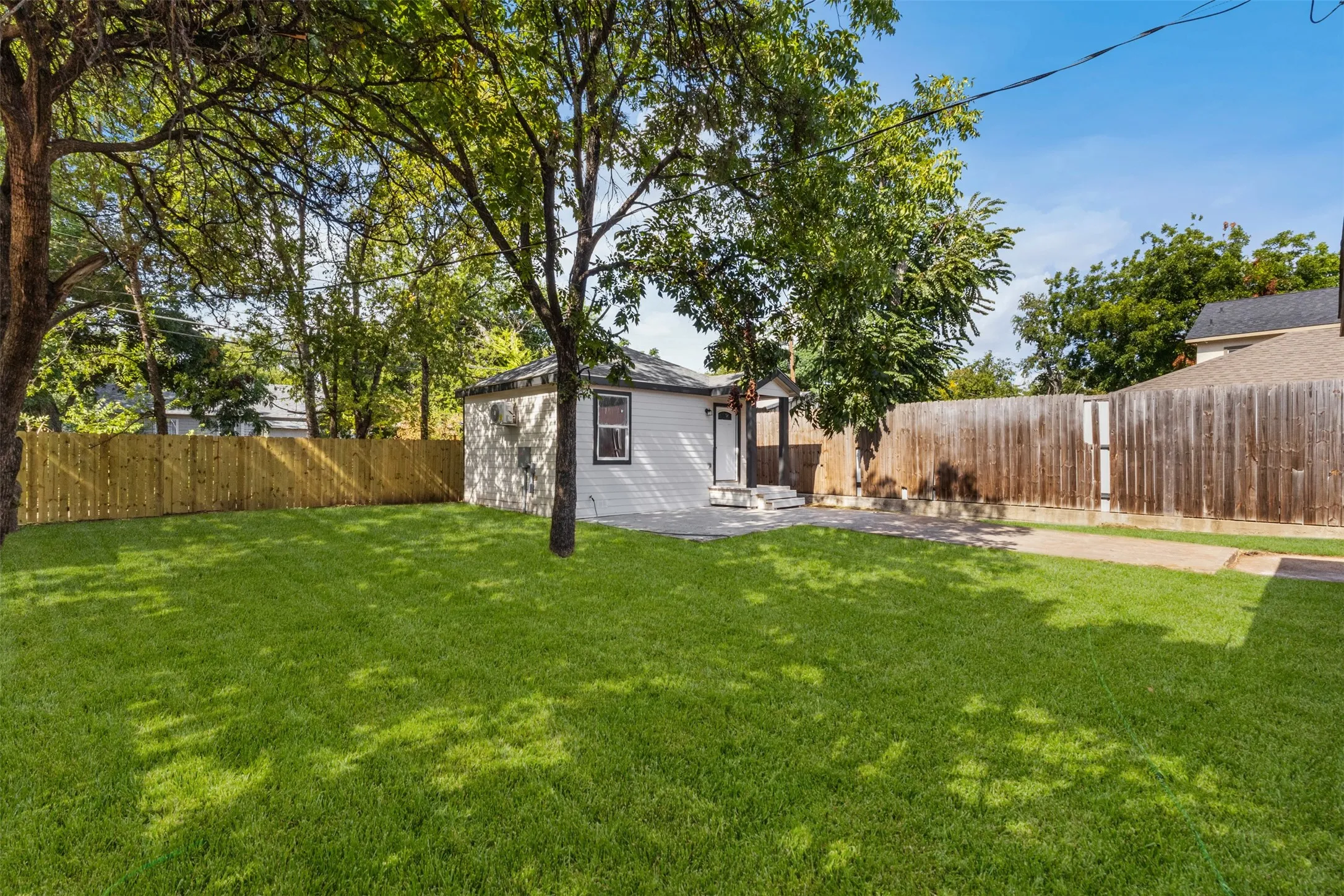 Expansive lawn featuring mature trees, a privacy fence, and a white exterior structure with a dark roof