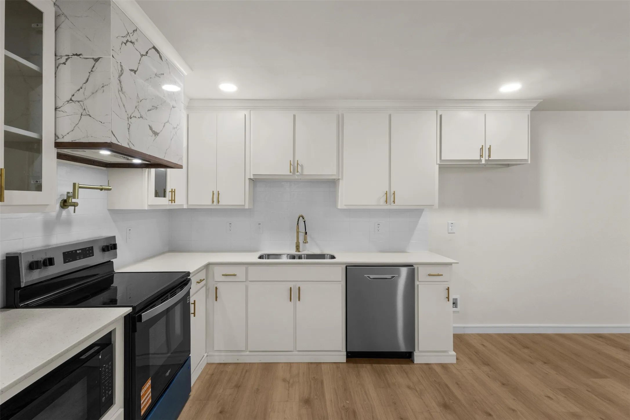 Kitchen featuring white cabinetry, quartz countertops, stainless steel appliances, wood-finish flooring, and a marble-patterned range hood