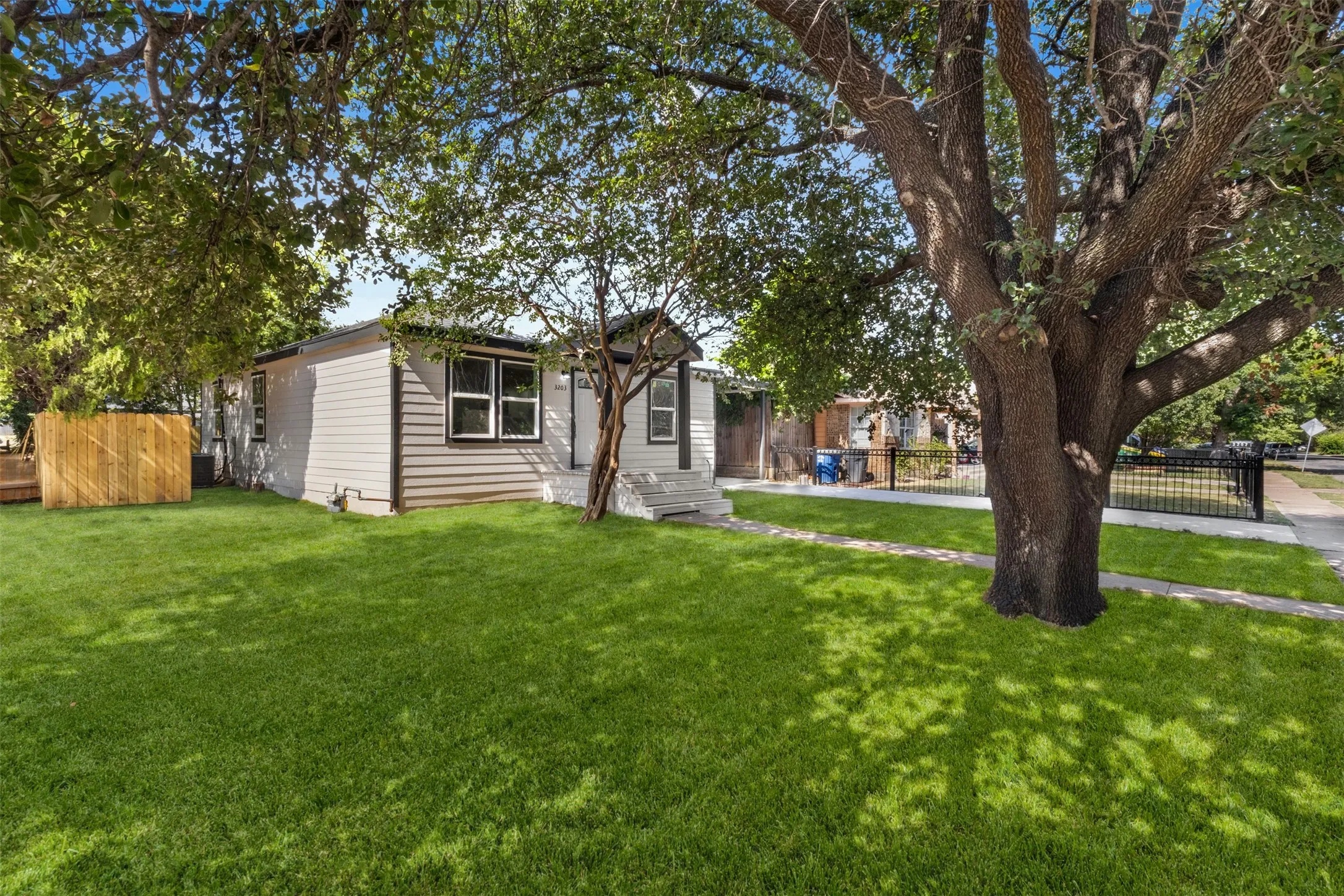 Front exterior with horizontal siding, multiple windows with dark trim, a mature tree, and a concrete pathway