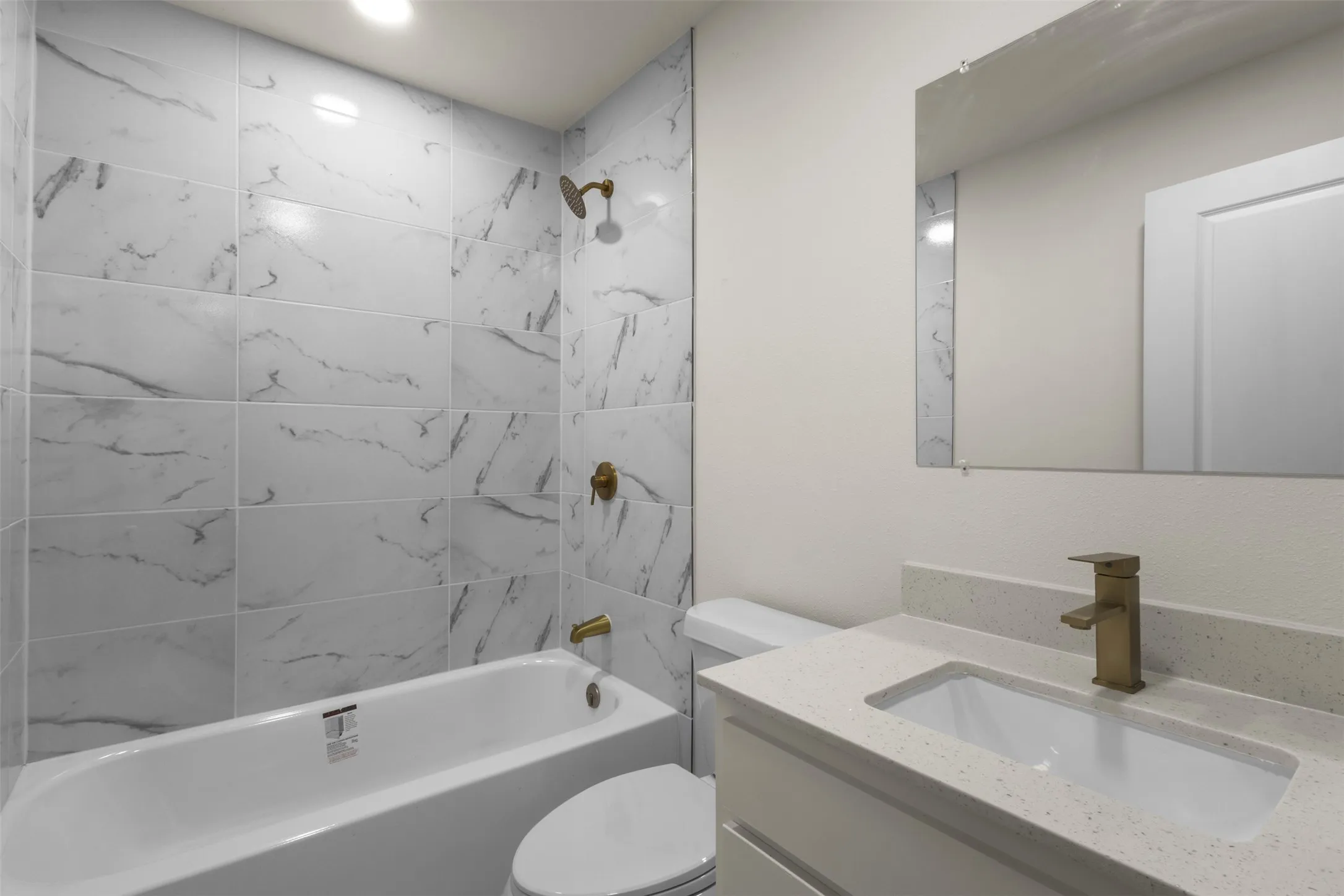 Bathroom featuring a white bathtub, large format marble-look tile surround, vanity with a rectangular sink, bronze-finish fixtures, and a frameless mirror