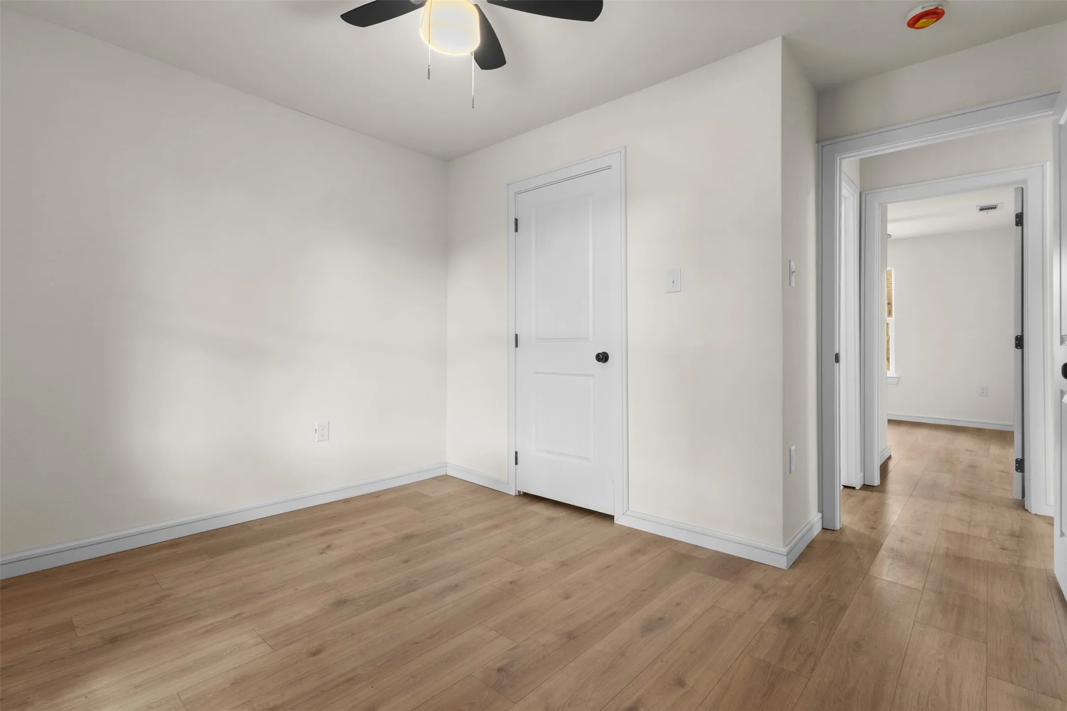 Wood-finish flooring with white baseboards, a white door with a black knob, and a ceiling fan with integrated lighting